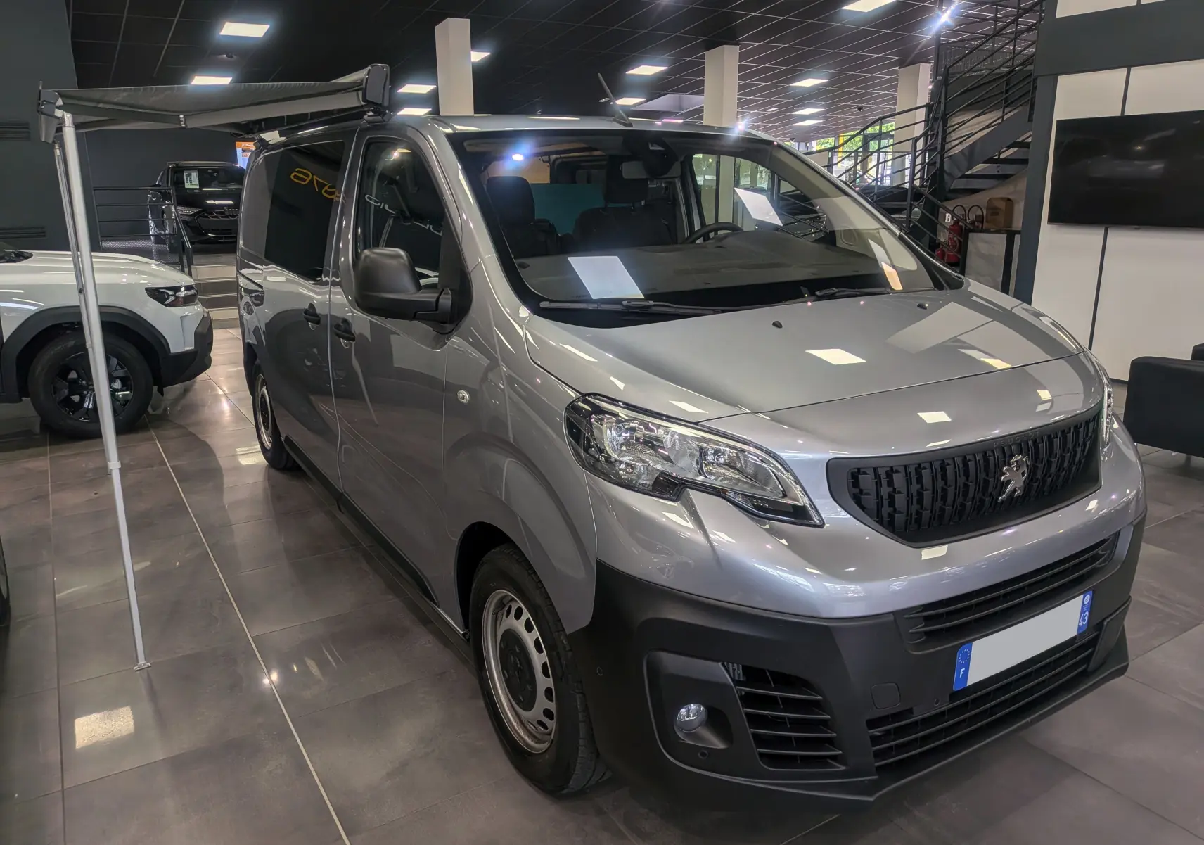 PEUGEOT Expert Fourgon gris acier vu en 3/4 avant droit, avec store Omnistor et aménagement intérieur visible.