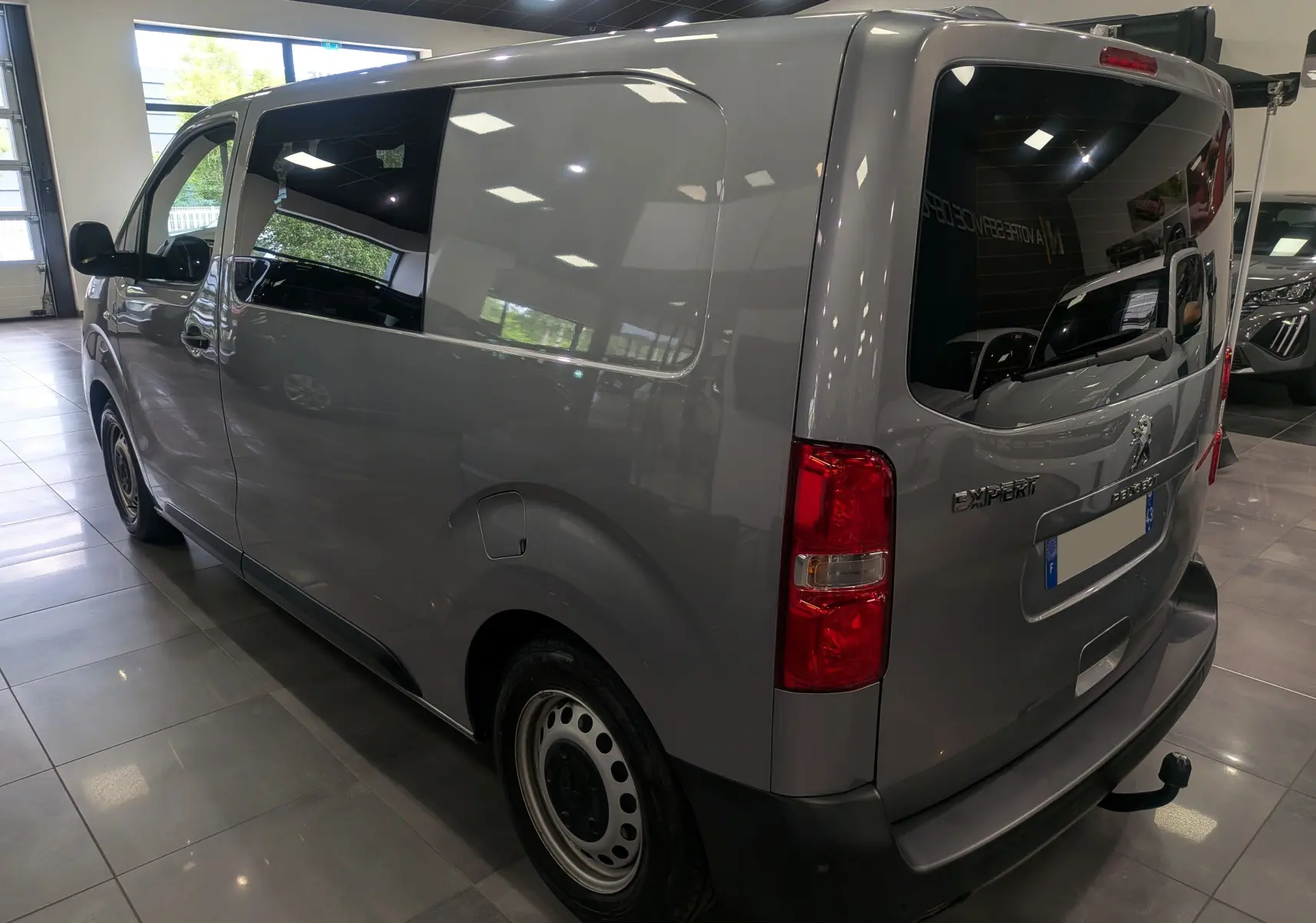 Vue 3/4 arrière droite du Peugeot Expert Fourgon gris acier 2023 aménagé avec store Omnistor et habillage bois visible.