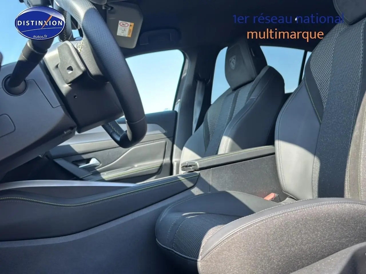 Intérieur avant droit de la Peugeot 308 gris, sièges sport avec surpiqûres vertes et accoudoir central visible.