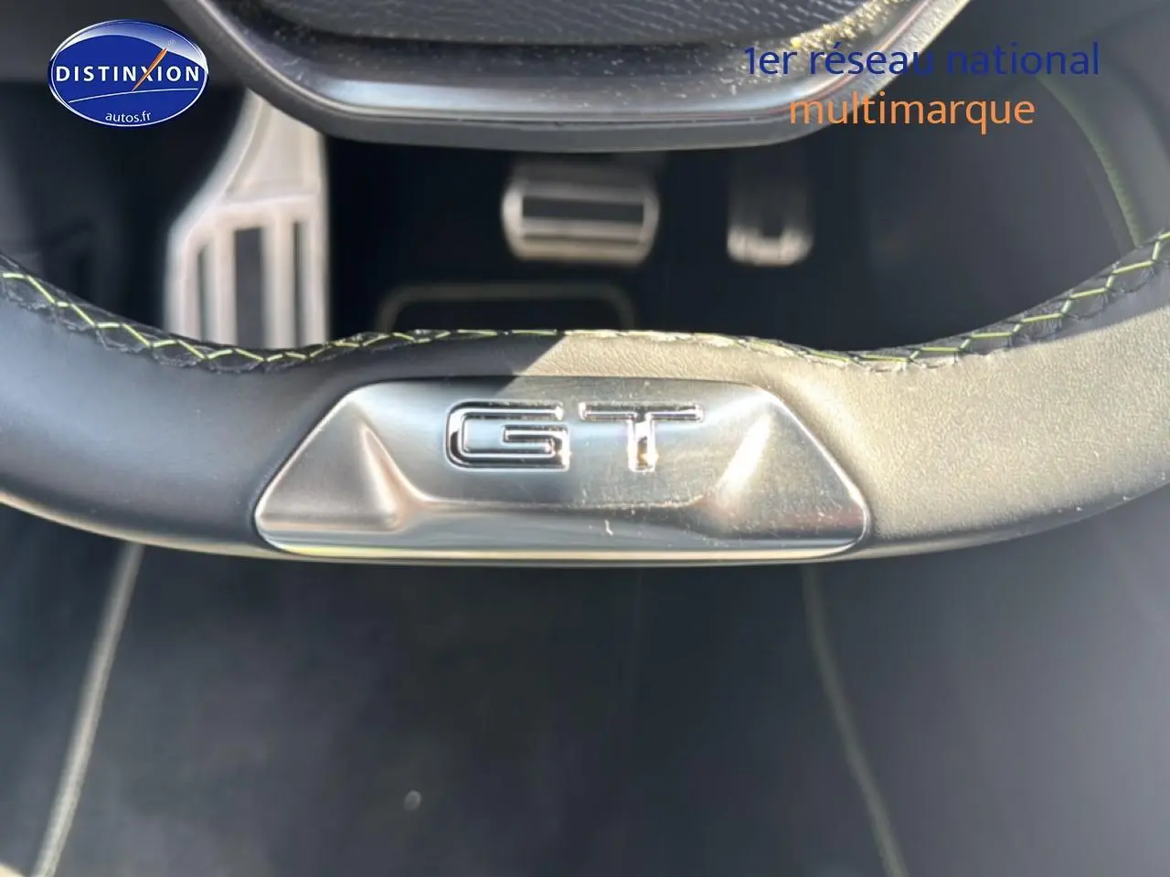 Gros plan sur le bas du volant noir avec logo GT argenté dans une Peugeot 308 gris, vue intérieure côté conducteur.