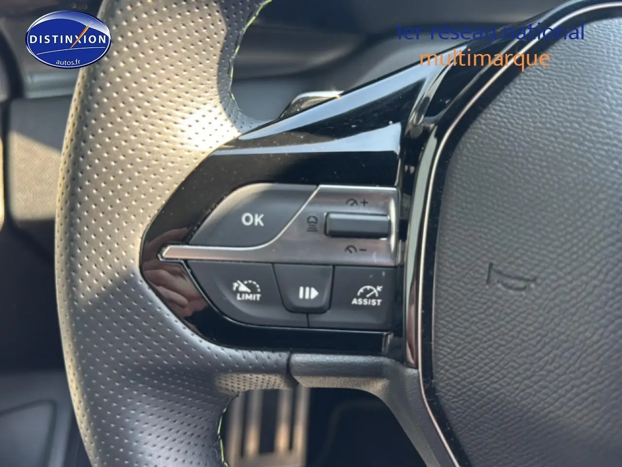Gros plan sur les commandes multifonctions à gauche du volant perforé gris d'une Peugeot 308 1.2 hybrid 145 GT 2025.