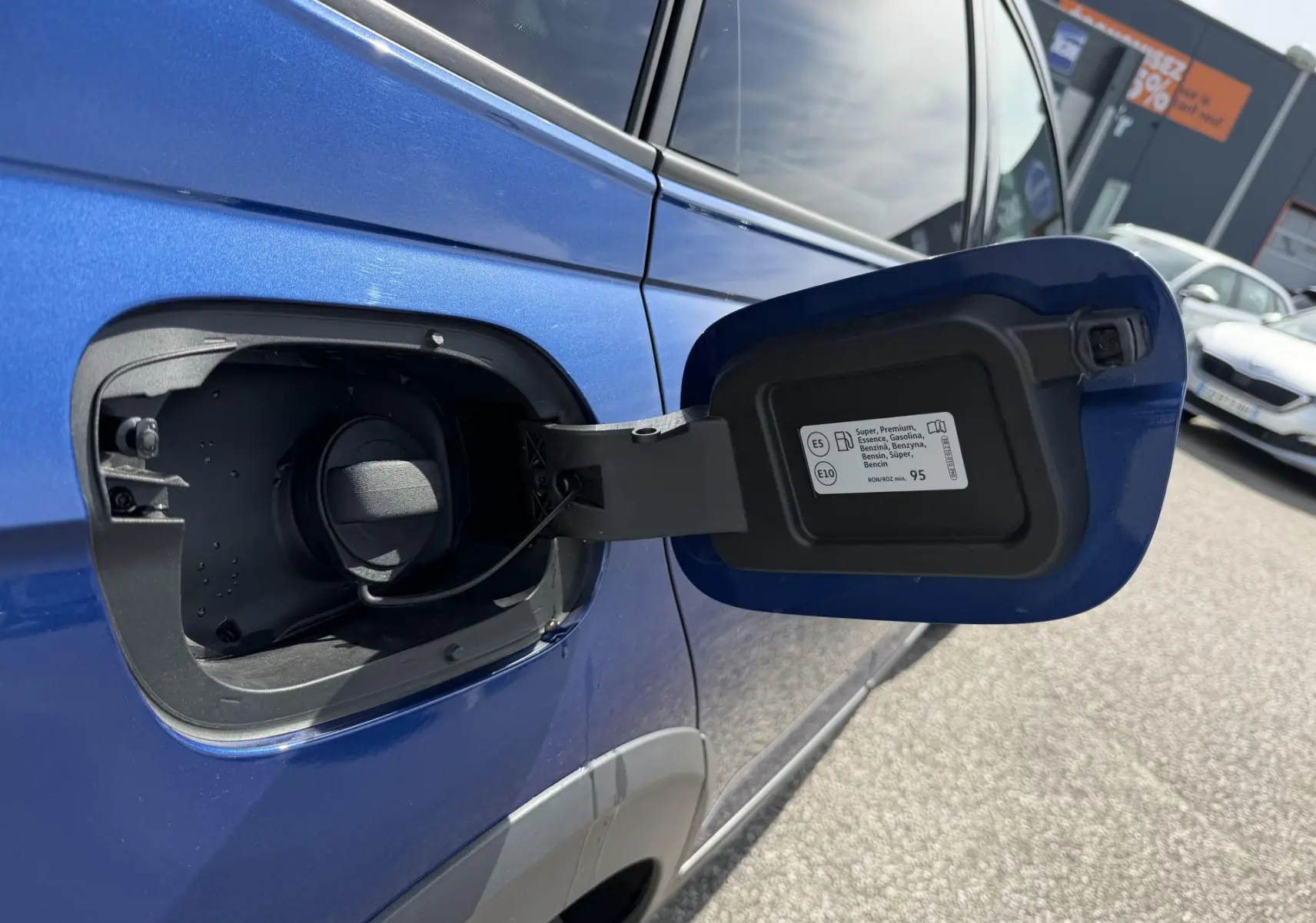 Vue rapprochée de la trappe à carburant ouverte côté gauche d’un Volkswagen Taigo bleu métallisé.