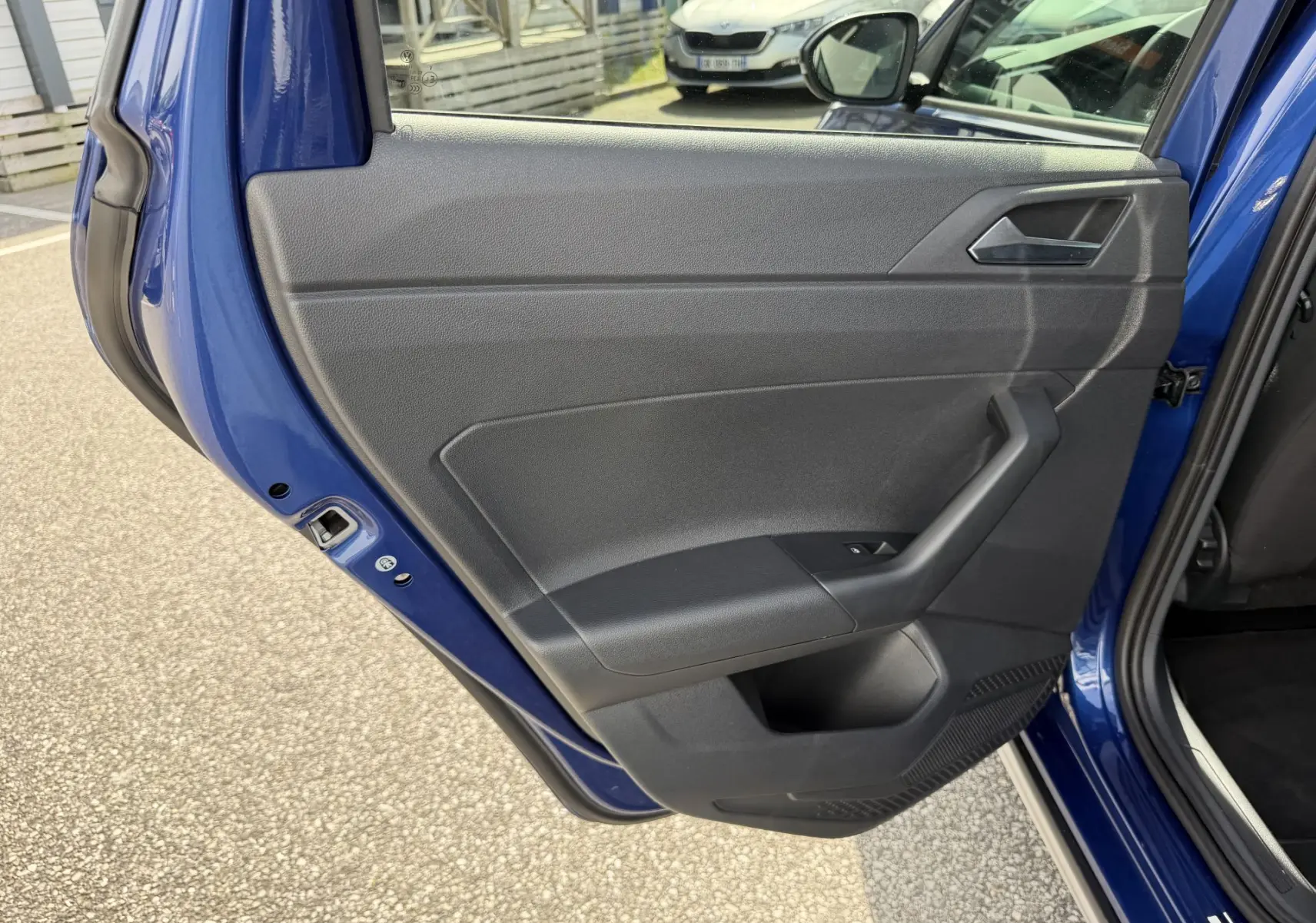 Vue rapprochée de la porte arrière gauche bleu métallisé du Volkswagen Taigo avec garniture intérieure noire et poignée intégrée.