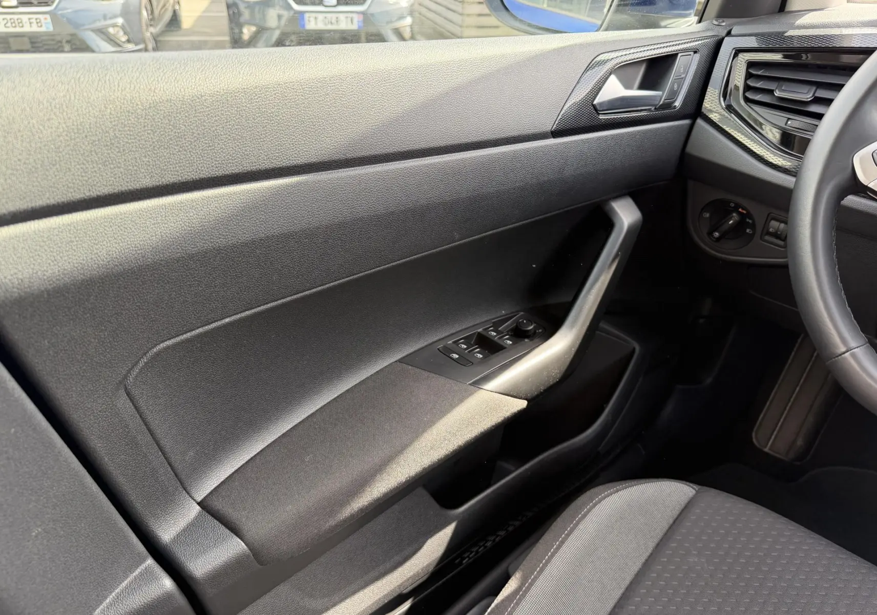 Intérieur côté conducteur du Volkswagen Taigo 2025, montrant la portière noire avec commandes des vitres et partie du volant cuir multifonctions.