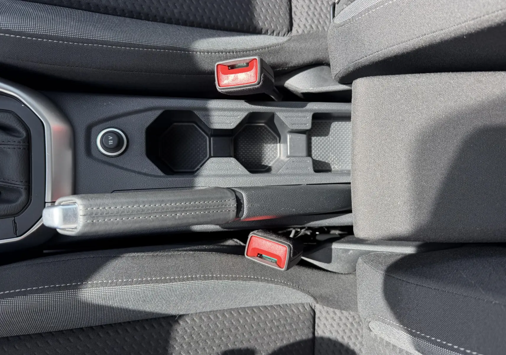 Vue plongeante sur la console centrale noire du Volkswagen Taigo avec frein à main manuel et porte-gobelets.