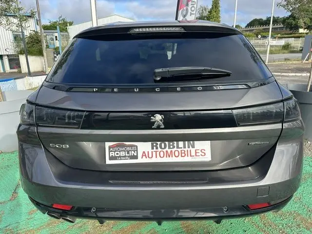 Vue arrière d'une Peugeot 508 SW gris métallisé avec logo lion et feux arrière noirs intégrés sur un parking.