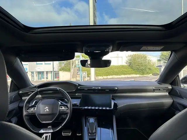 Vue intérieure avant du Peugeot 508 SW gris 2020, avec volant compact, tableau de bord moderne et toit ouvrant panoramique.