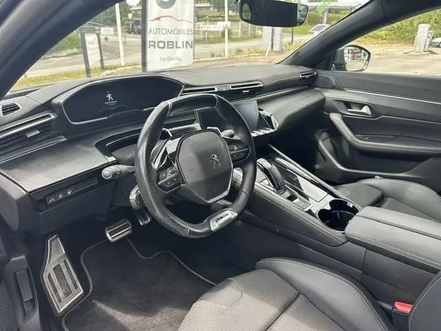 Vue intérieure côté conducteur de la Peugeot 508 SW 2020, tableau de bord noir avec volant compact et console centrale moderne.