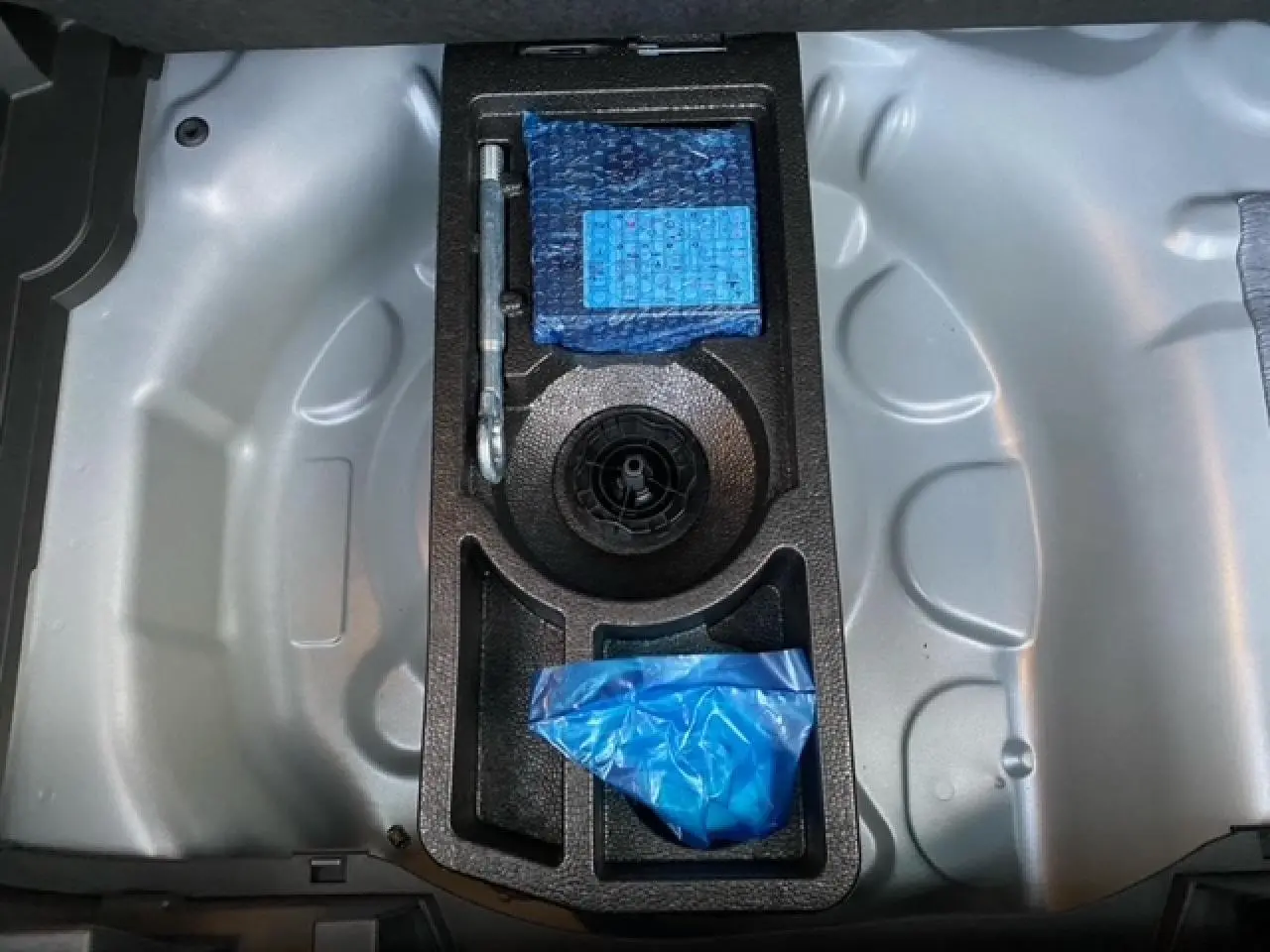 Coffre de l'Opel Crossland gris alu 2022 montrant le rangement sous le plancher avec outils et accessoires emballés.