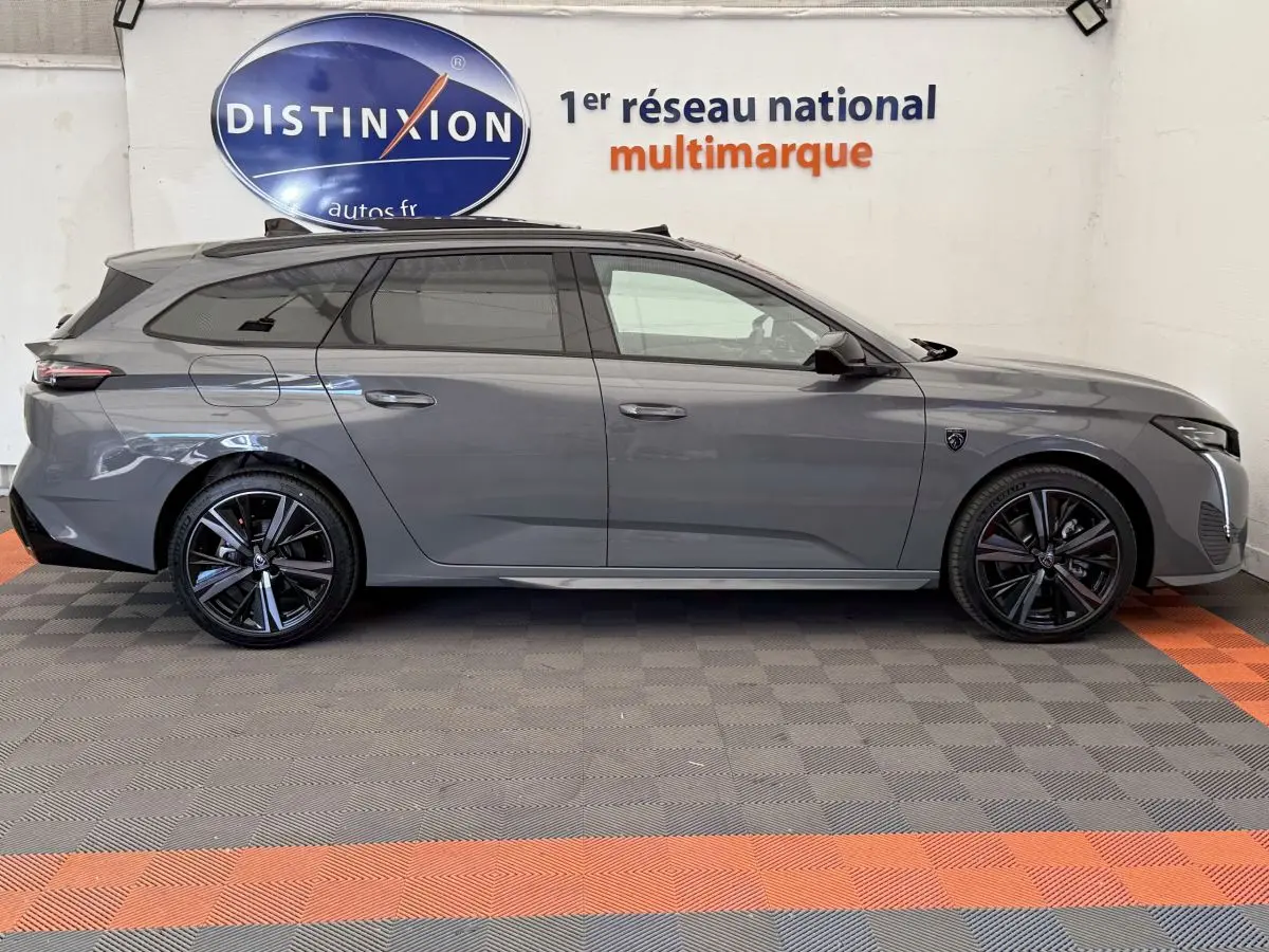 Profil droit d'une Peugeot 308 Hybrid 136 e-DCS6 GT gris foncé avec jantes noires et toit panoramique visible.