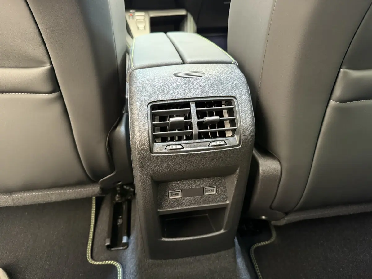 Vue rapprochée des aérateurs arrière et ports USB entre les sièges avant noirs d'une Peugeot 308 Hybrid 2024 gris foncé.