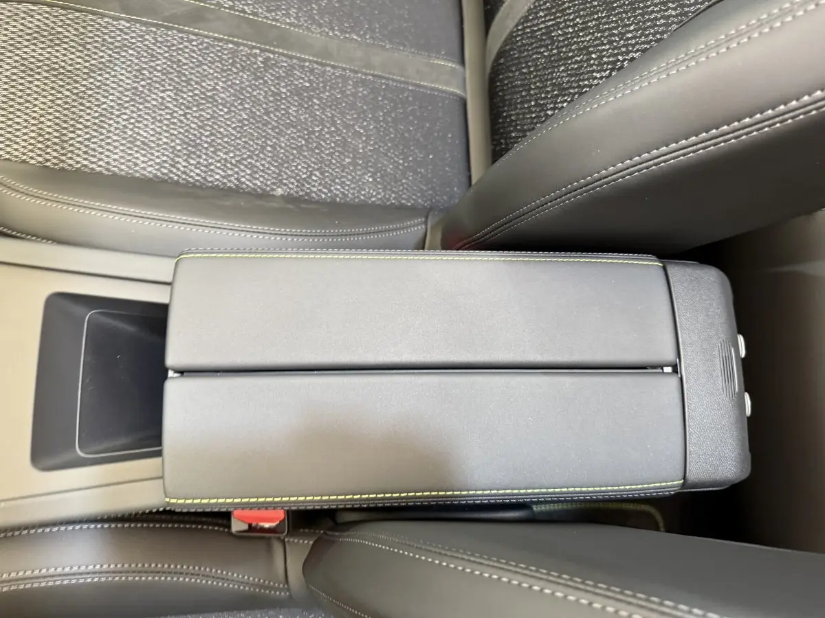 Vue rapprochée de l'accoudoir central gris foncé avec surpiqûres vertes à l'intérieur d'une Peugeot 308 Hybrid 136 e-DCS6 GT 2024.