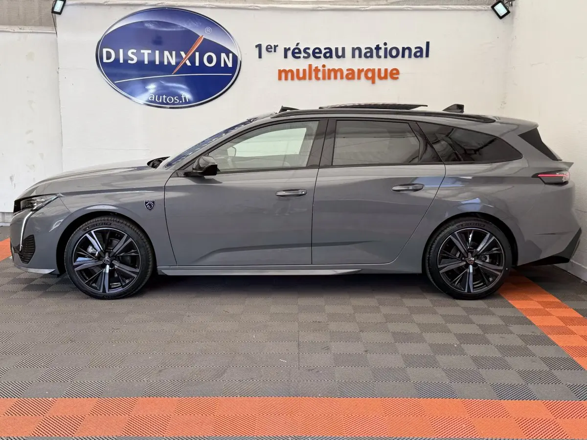 Profil droit d'une Peugeot 308 Hybrid 136 e-DCS6 GT gris foncé avec jantes noires et toit ouvrant en intérieur showroom.