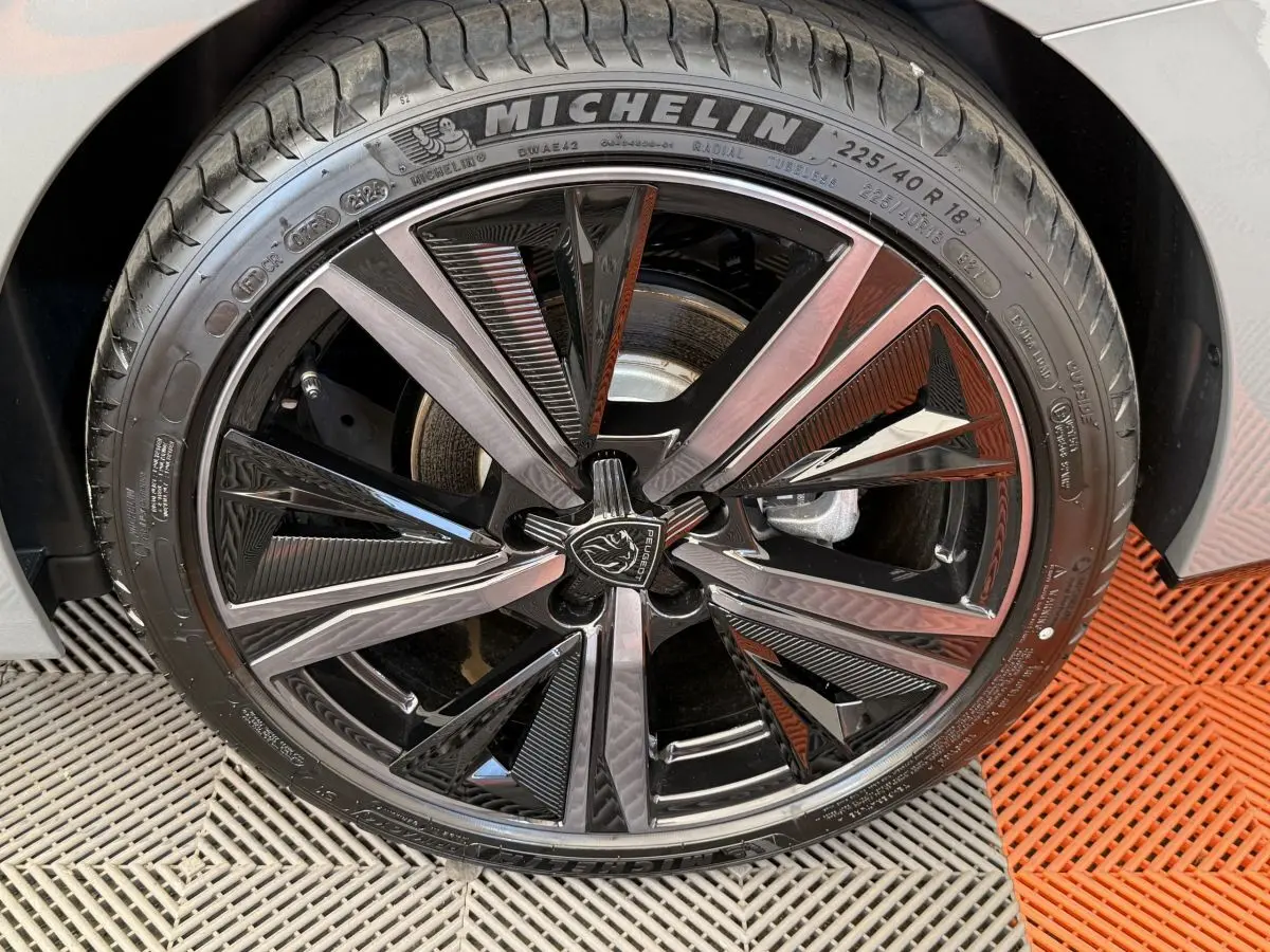 Gros plan sur la jante noire et argentée avec logo Peugeot de la roue avant droite d'une 308 Hybrid 136 e-DCS6 GT gris foncé.