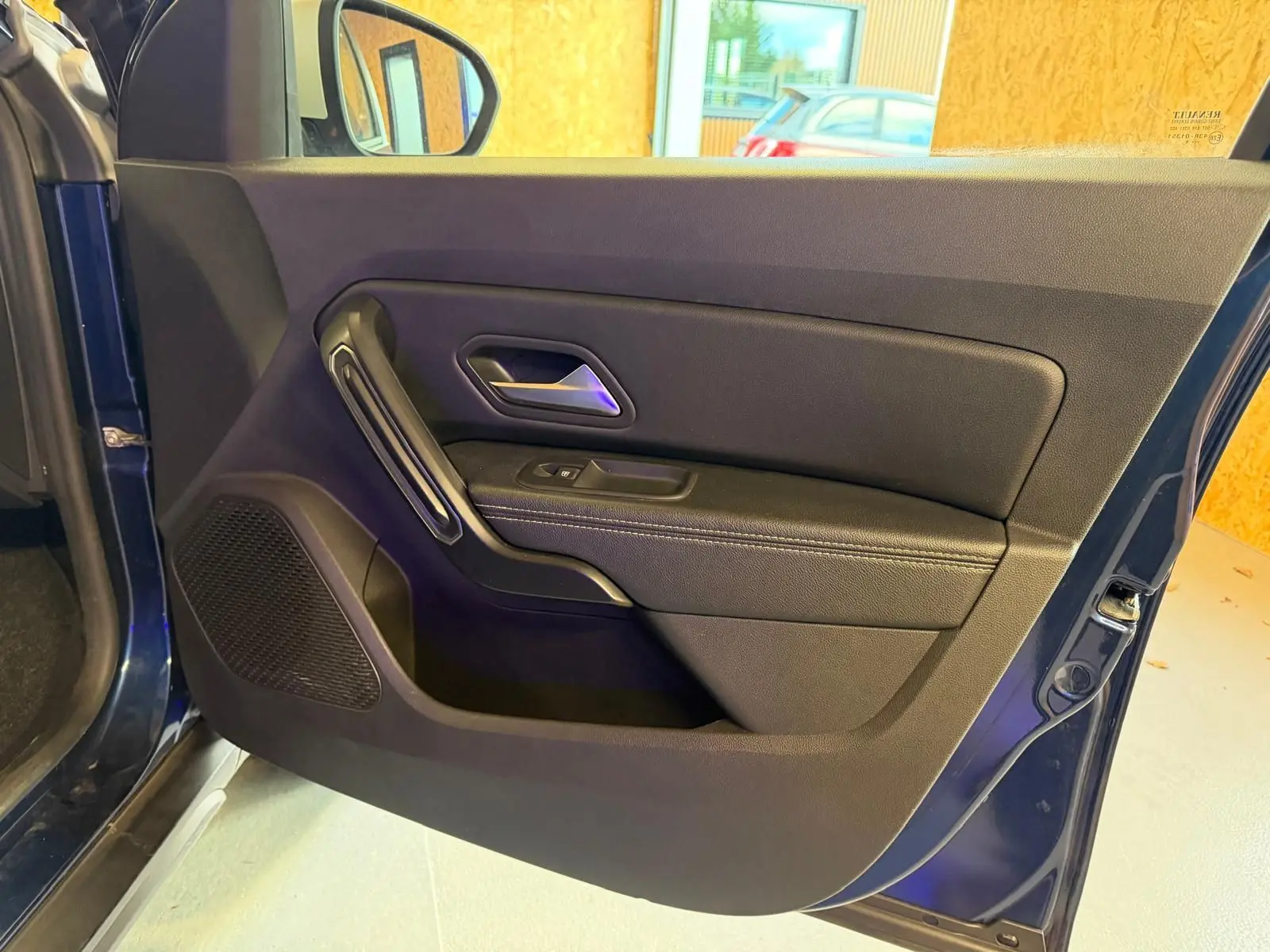Vue intérieure de la porte avant gauche bleu foncé du Dacia Duster avec poignée et commande de vitre électrique.