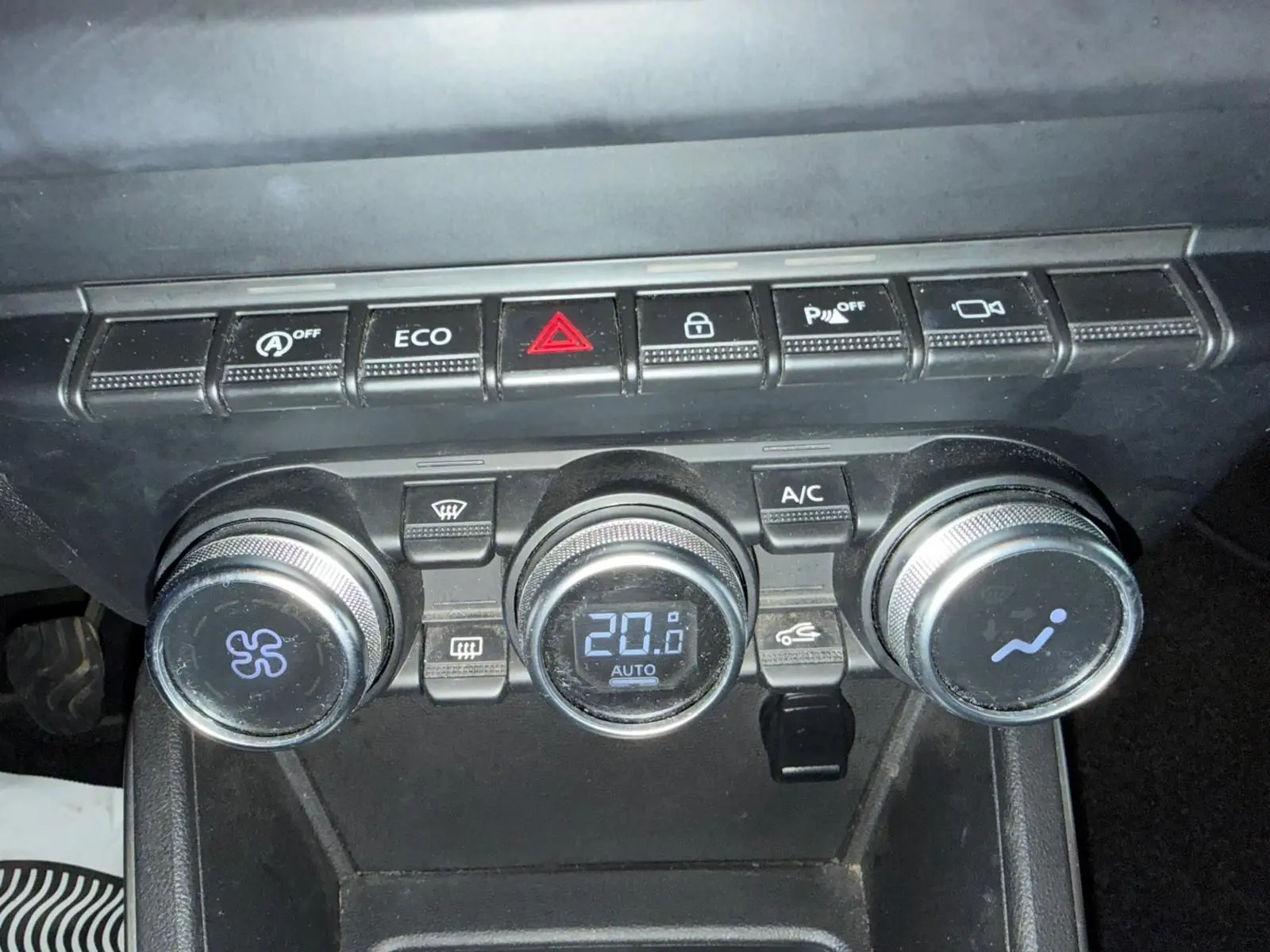 Gros plan sur la console centrale noire du Dacia Duster bleu, montrant les commandes de climatisation automatique et boutons fonctionnels.