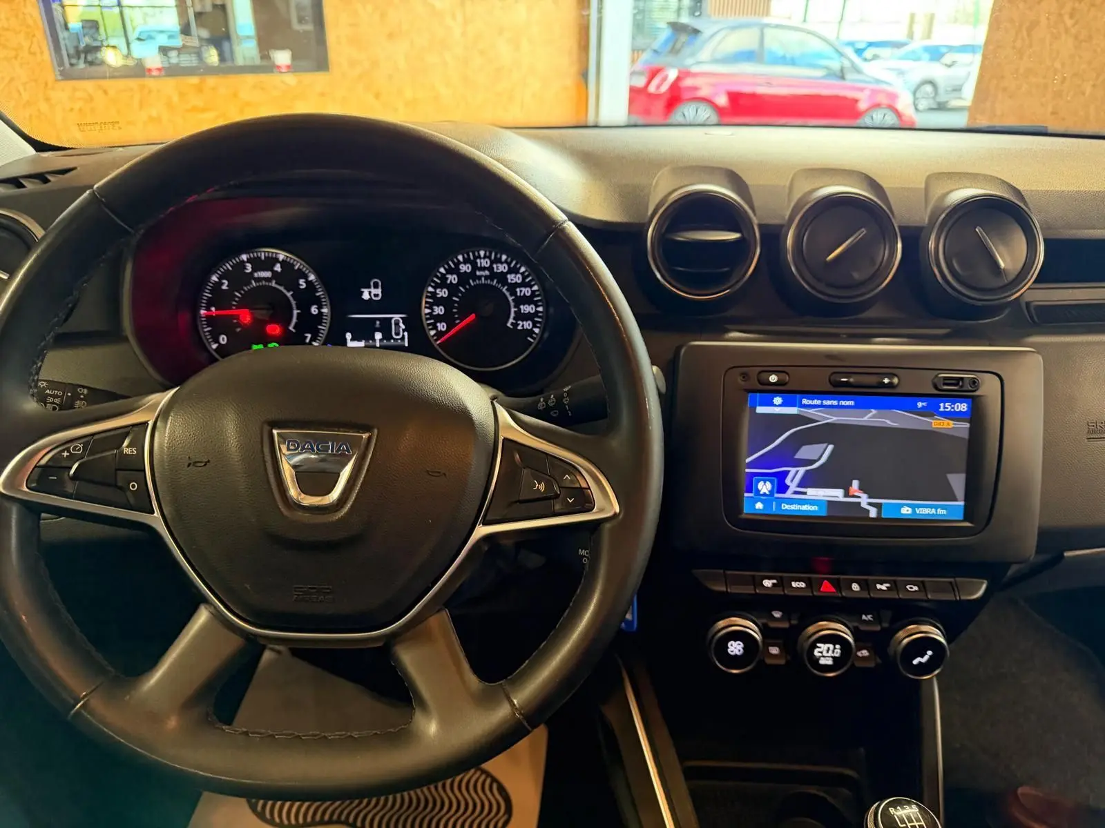 Vue frontale de l'intérieur du Dacia Duster bleu, volant cuir avec commandes, tableau de bord et écran tactile GPS.