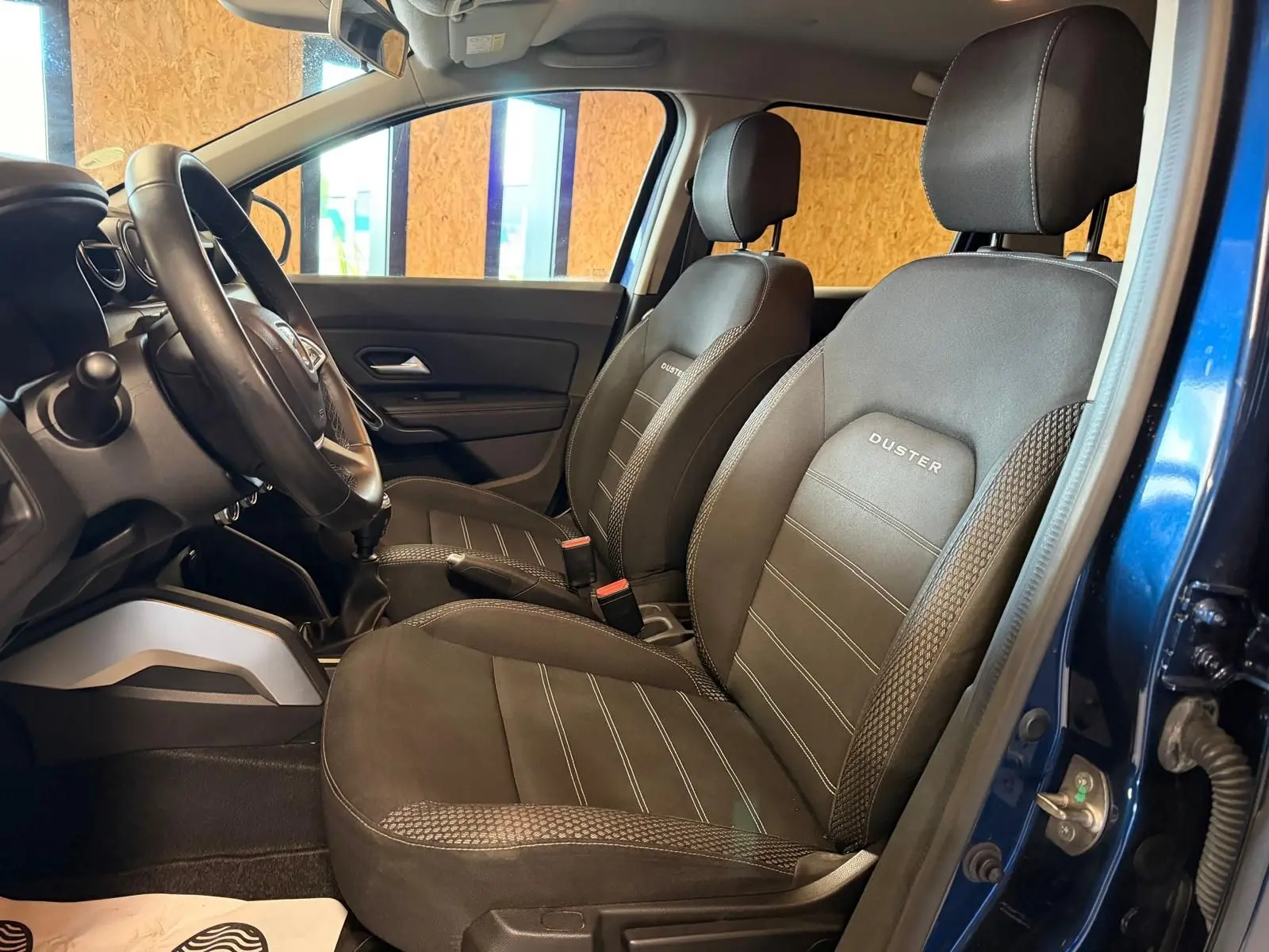 Intérieur du Dacia Duster bleu, vue côté gauche sur les sièges avant en tissu "Prestige" avec logo brodé.