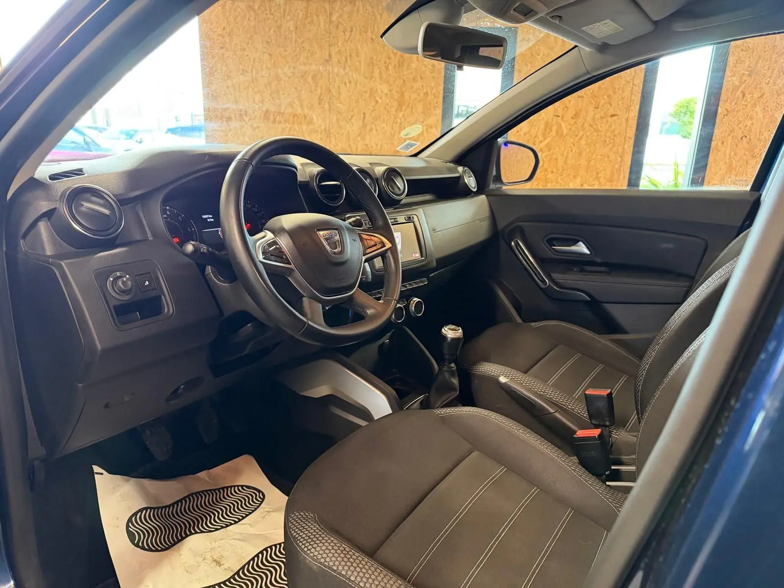 Intérieur avant droit du Dacia Duster bleu, volant multifonctions, sièges tissu Prestige et levier de vitesse manuel visible.