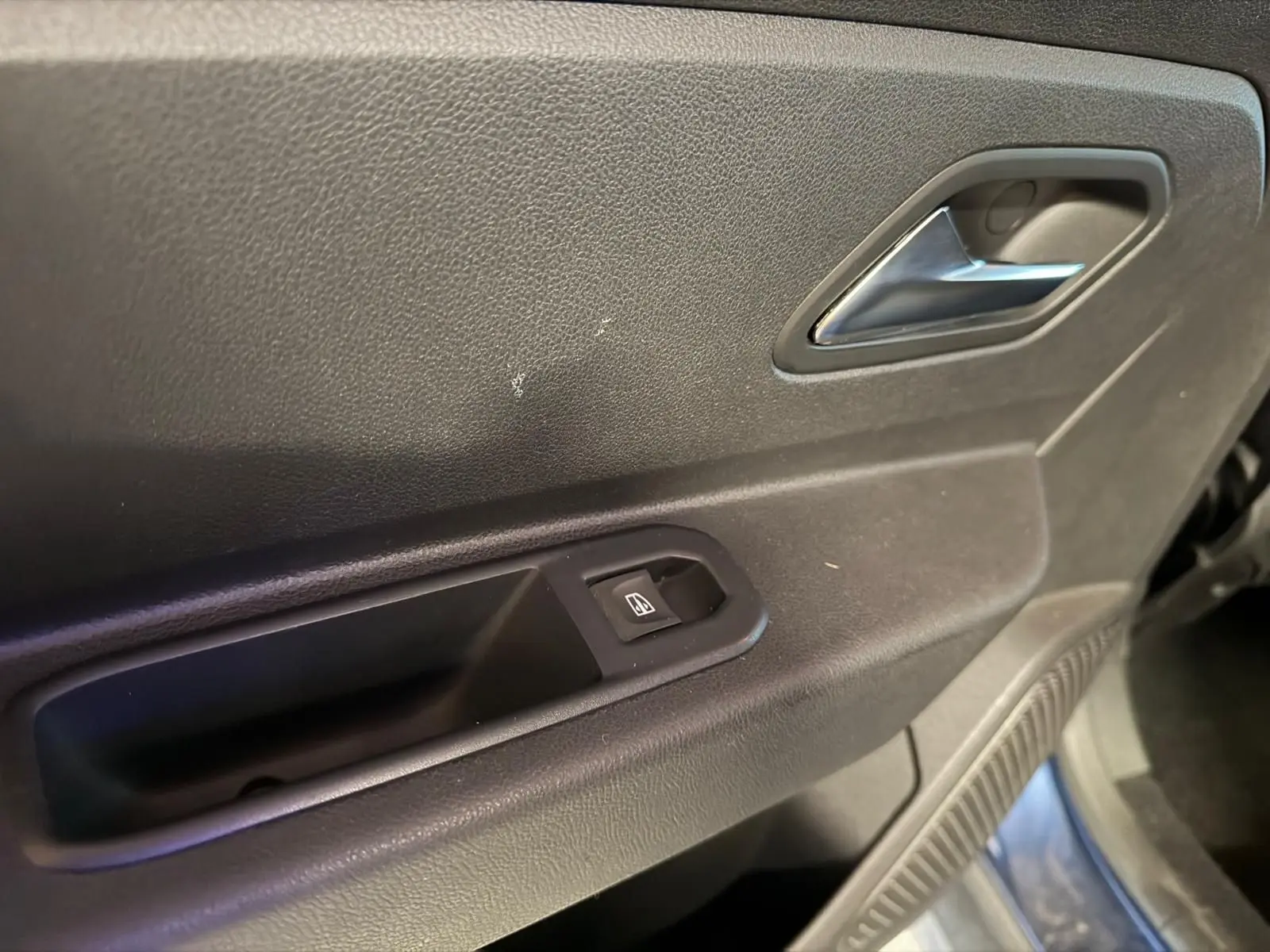 Gros plan sur la porte intérieure côté droit du Dacia Duster bleu, avec poignée argentée et bouton de lève-vitre.