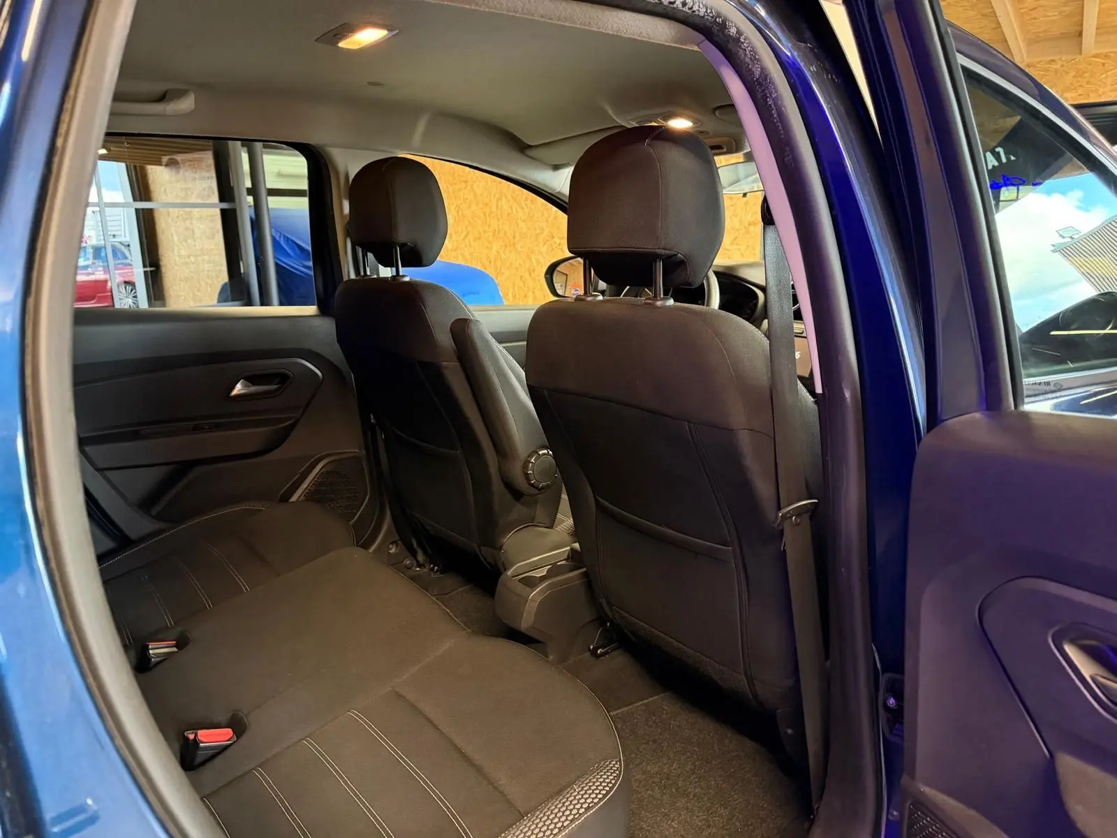 Intérieur arrière du Dacia Duster bleu, vue côté gauche avec sièges tissu noir et appuie-têtes virgulés.