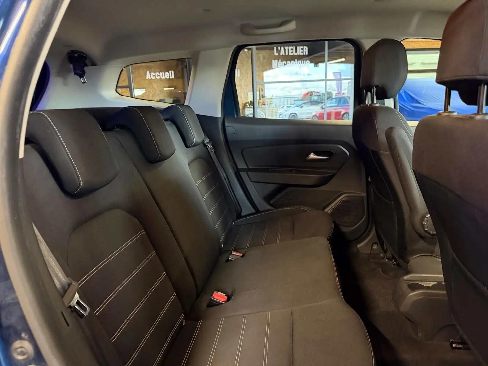 Vue intérieure côté gauche des sièges arrière noirs du Dacia Duster bleu, avec surpiqûres et appuie-têtes ajustés.