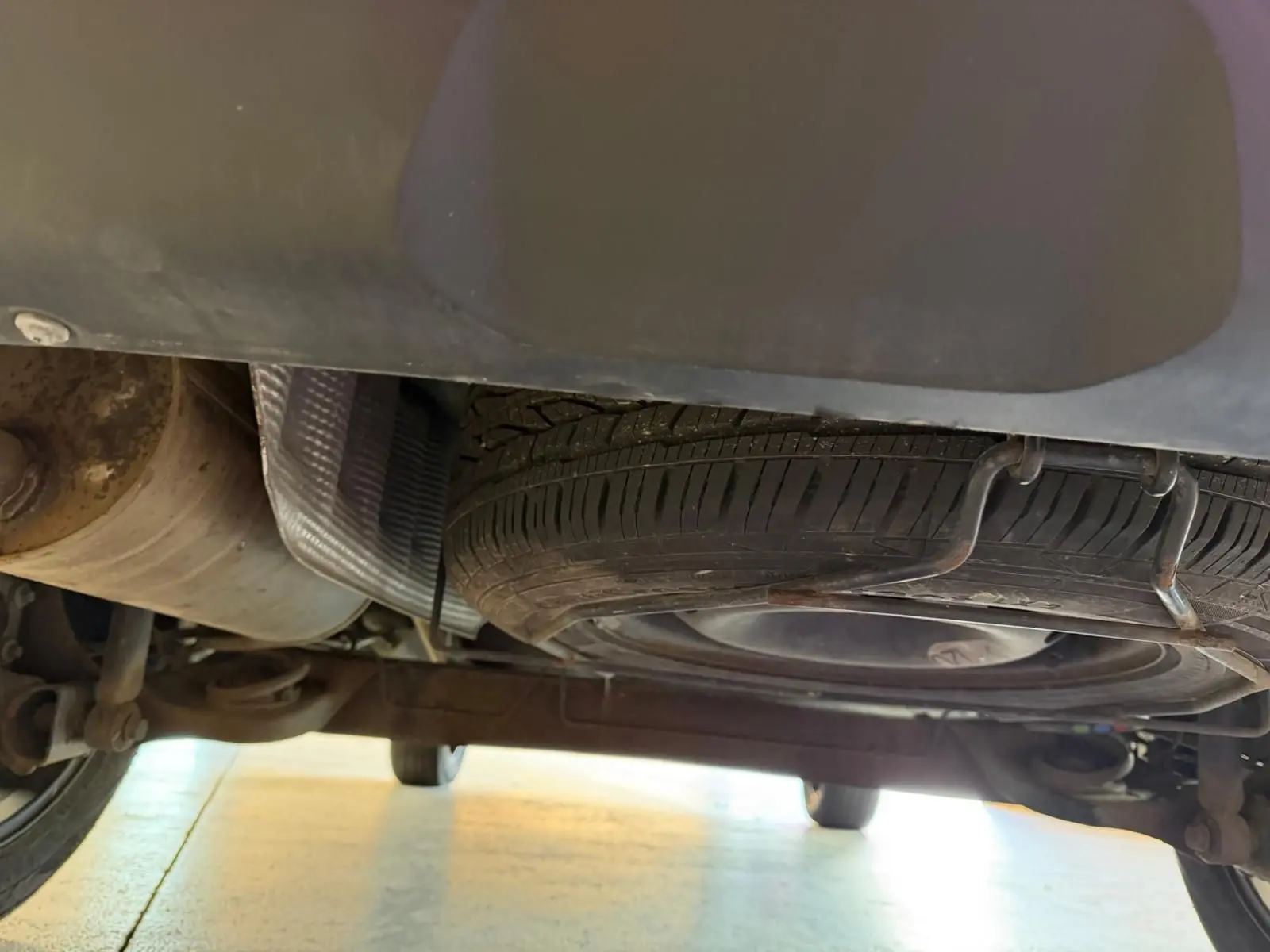 Vue sous le Dacia Duster bleu, montrant la roue de secours galette et le système d'échappement arrière.