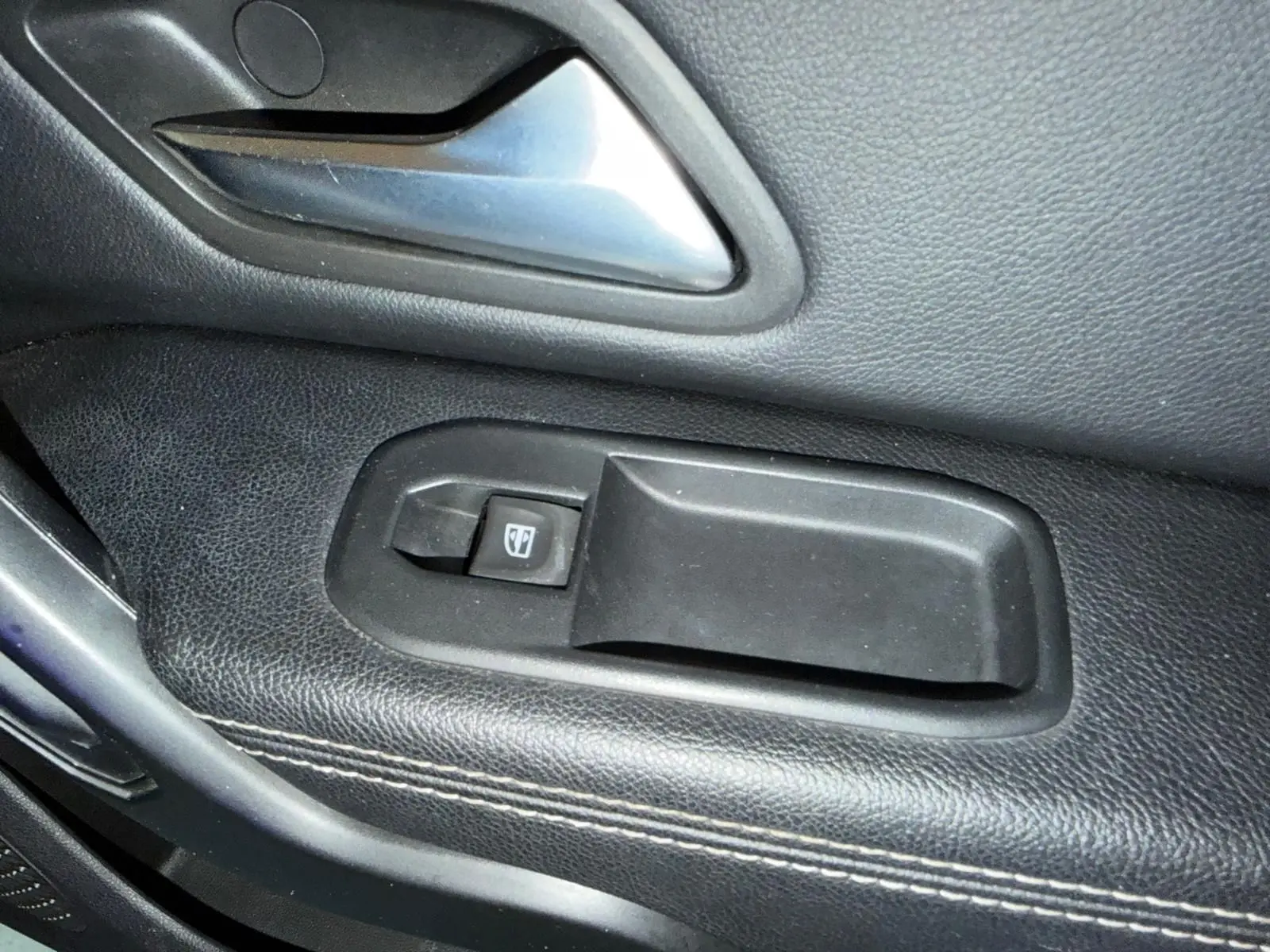 Gros plan sur la poignée intérieure et le bouton de lève-vitre côté gauche du Dacia Duster bleu Prestige.