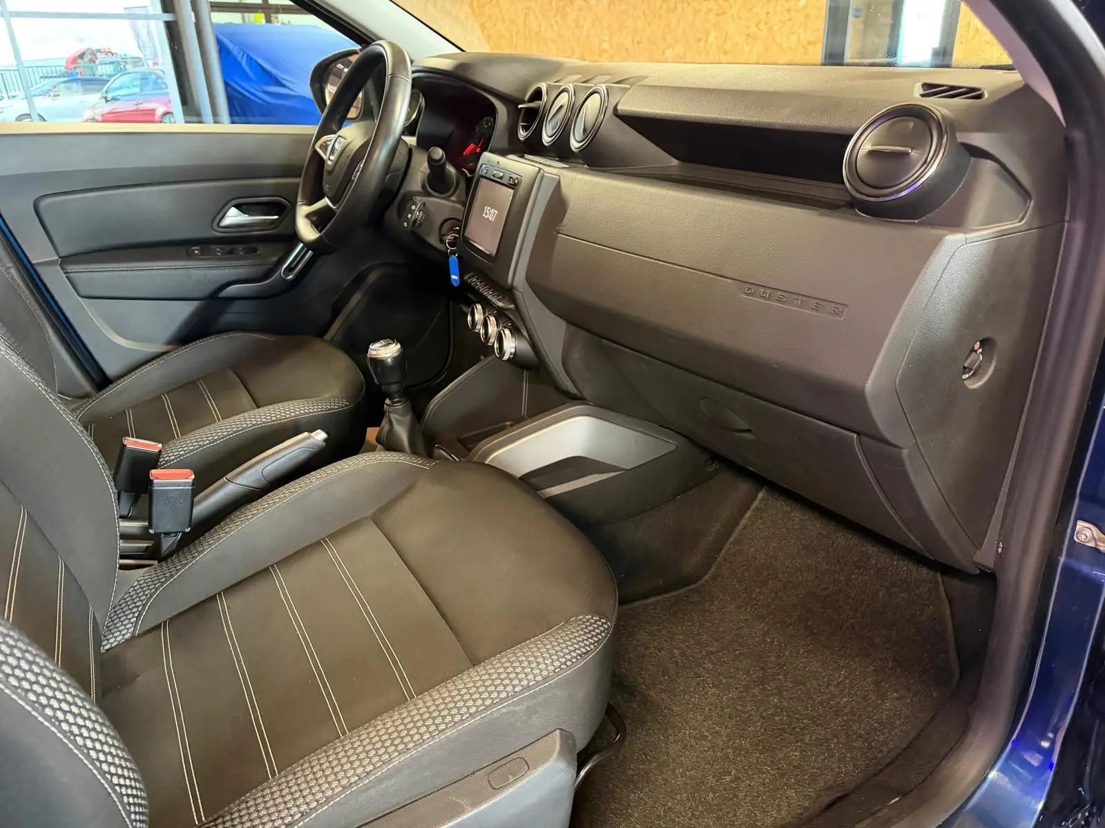 Intérieur avant droit du Dacia Duster bleu, avec tableau de bord noir, sièges tissu Prestige et volant réglable.