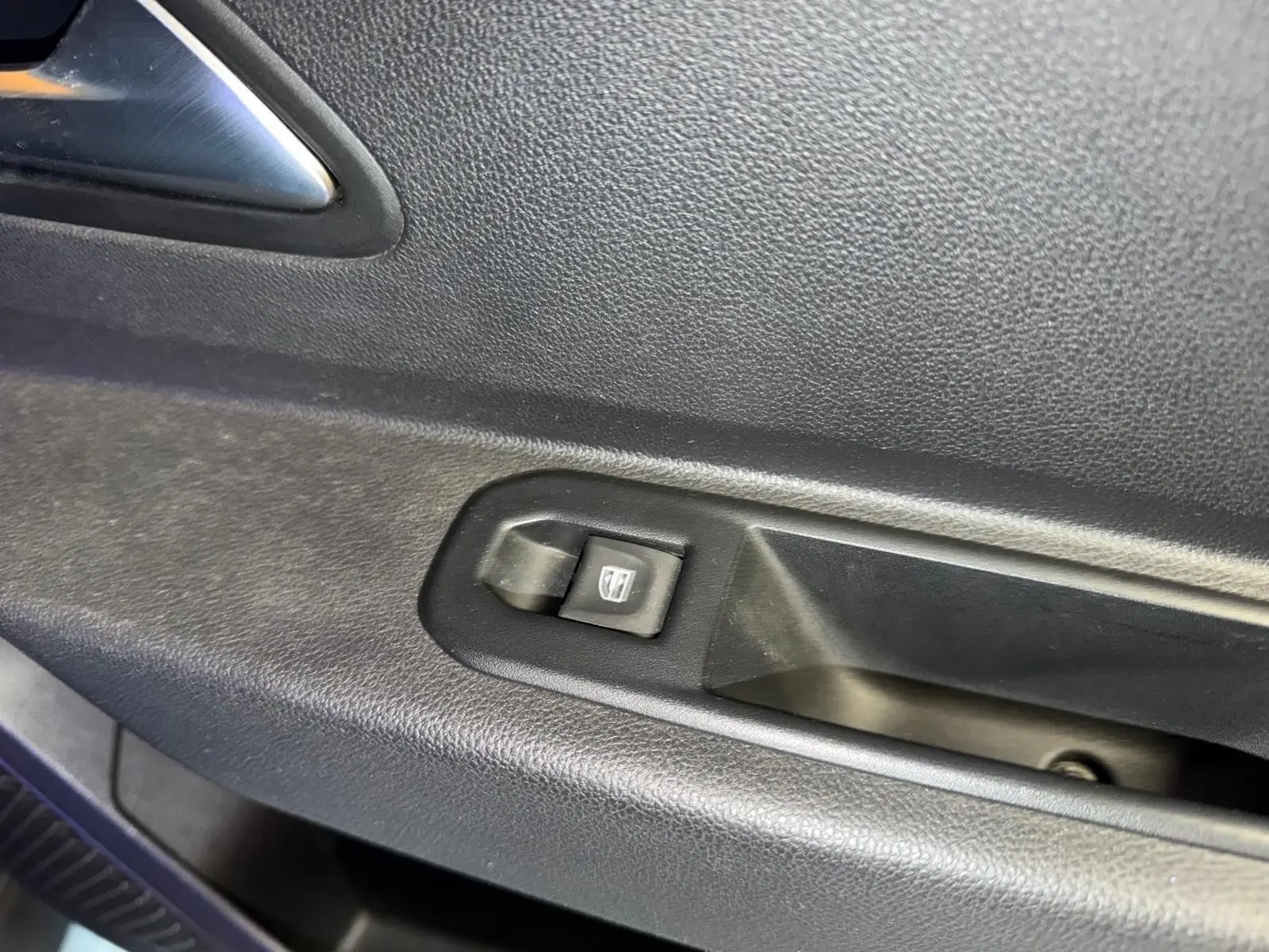 Gros plan sur le bouton de lève-vitre électrique côté gauche intérieur du Dacia Duster bleu Prestige.