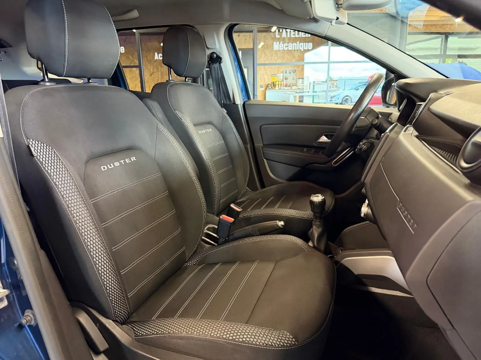 Intérieur du Dacia Duster bleu, vue côté droit sur sièges tissu Prestige noirs avec logo Duster brodé.
