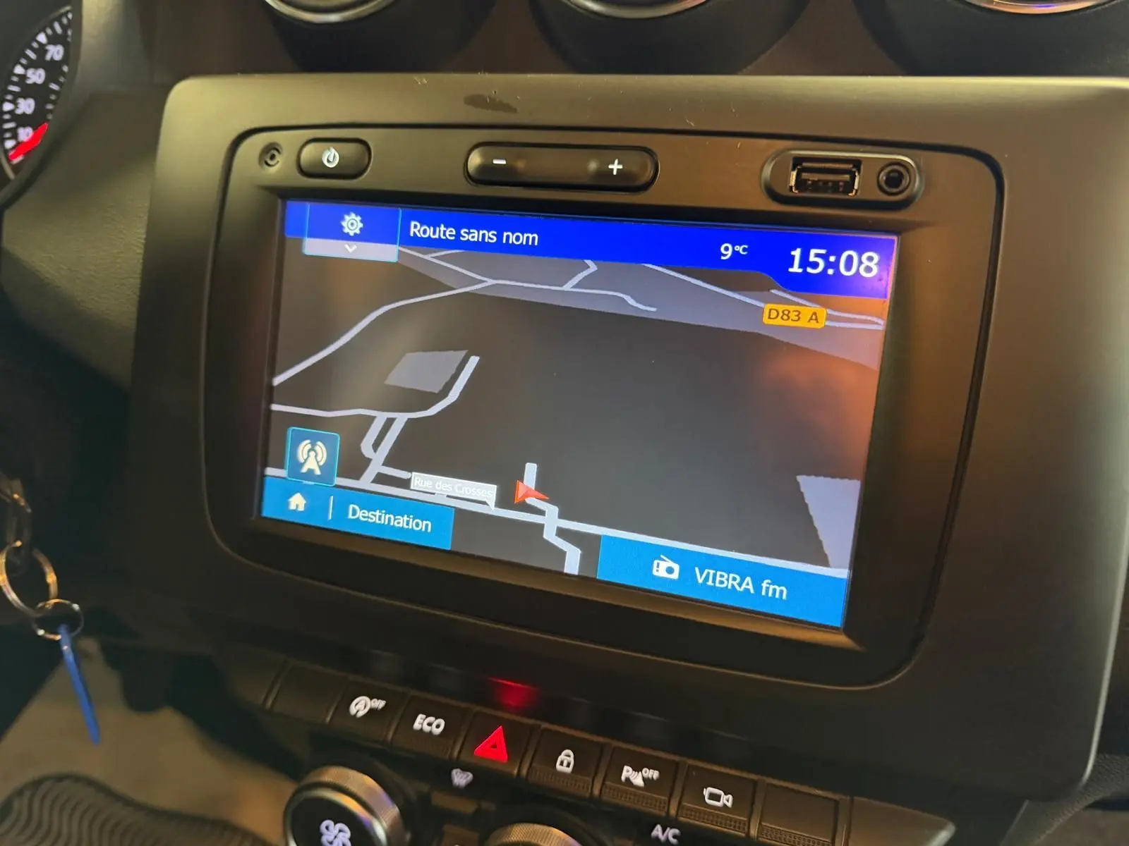 Écran tactile du GPS allumé dans le tableau de bord noir du Dacia Duster bleu, avec commandes climatisation et mode Eco visibles.
