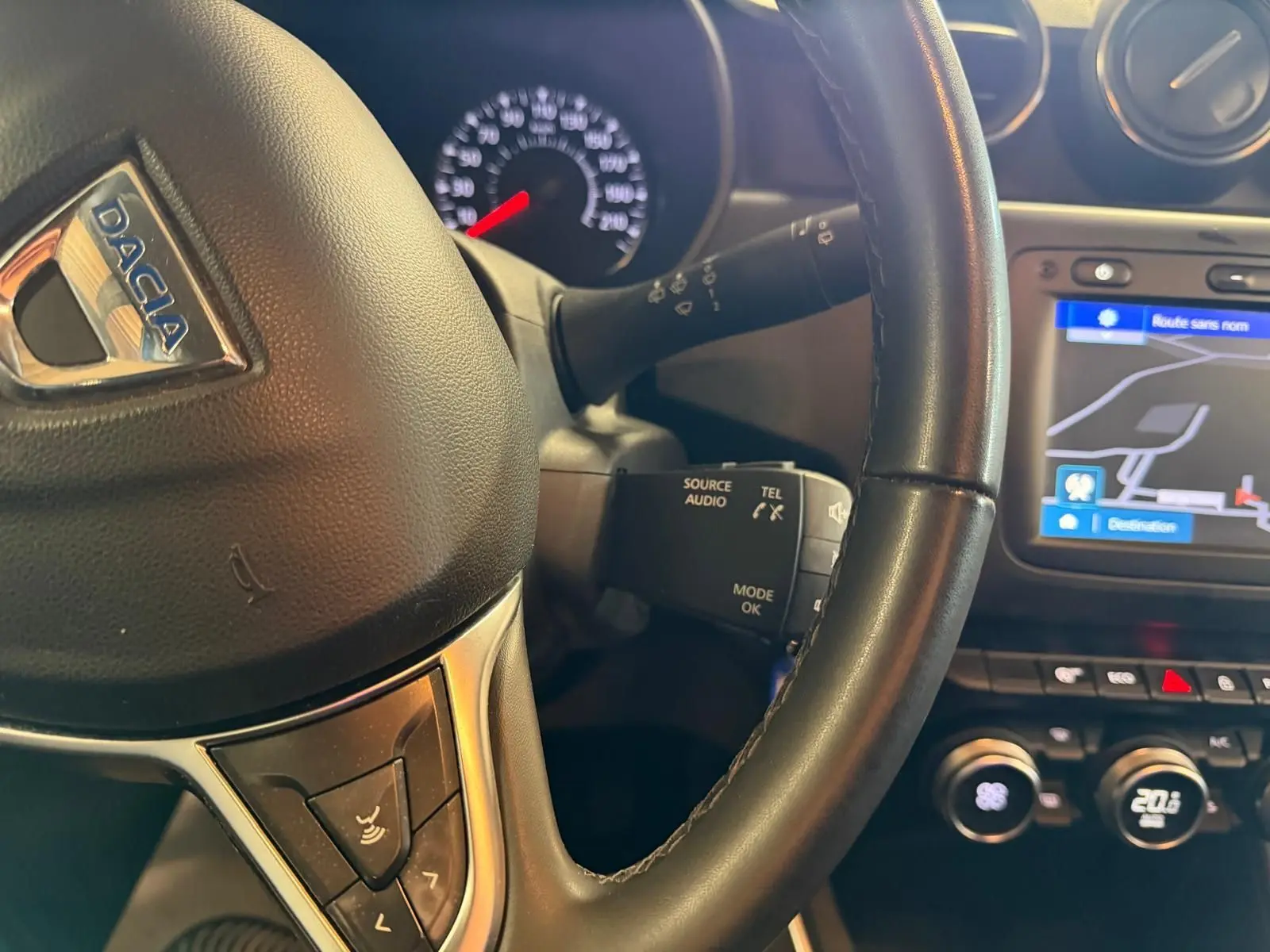 Gros plan sur le volant noir du Dacia Duster avec commandes audio et écran de navigation affichant une carte.