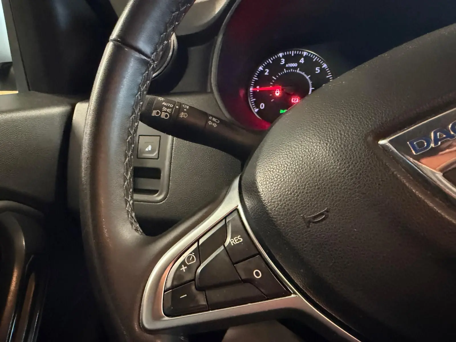 Gros plan sur le volant noir du Dacia Duster bleu, avec commandes intégrées et tableau de bord éclairé en arrière-plan.