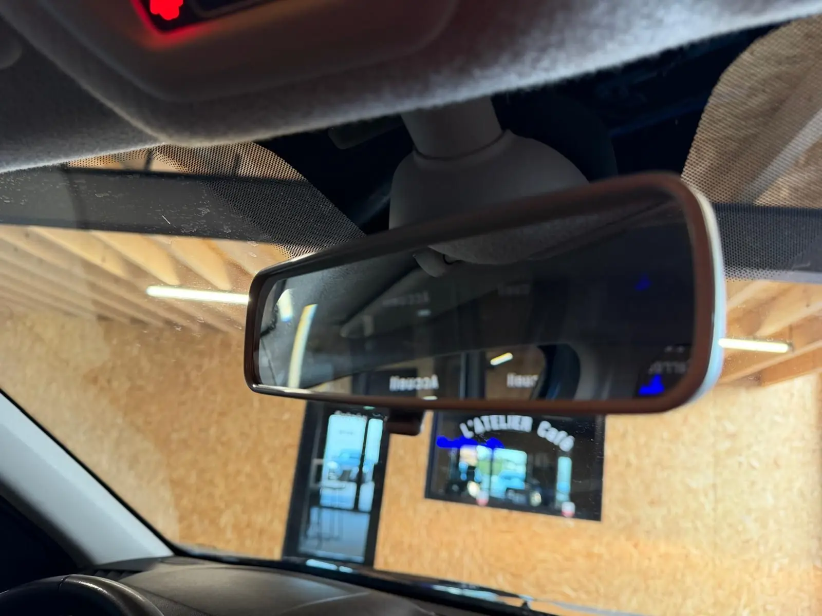 Rétroviseur intérieur du Dacia Duster bleu, vue rapprochée avec reflet d'une porte et d'un panneau lumineux.