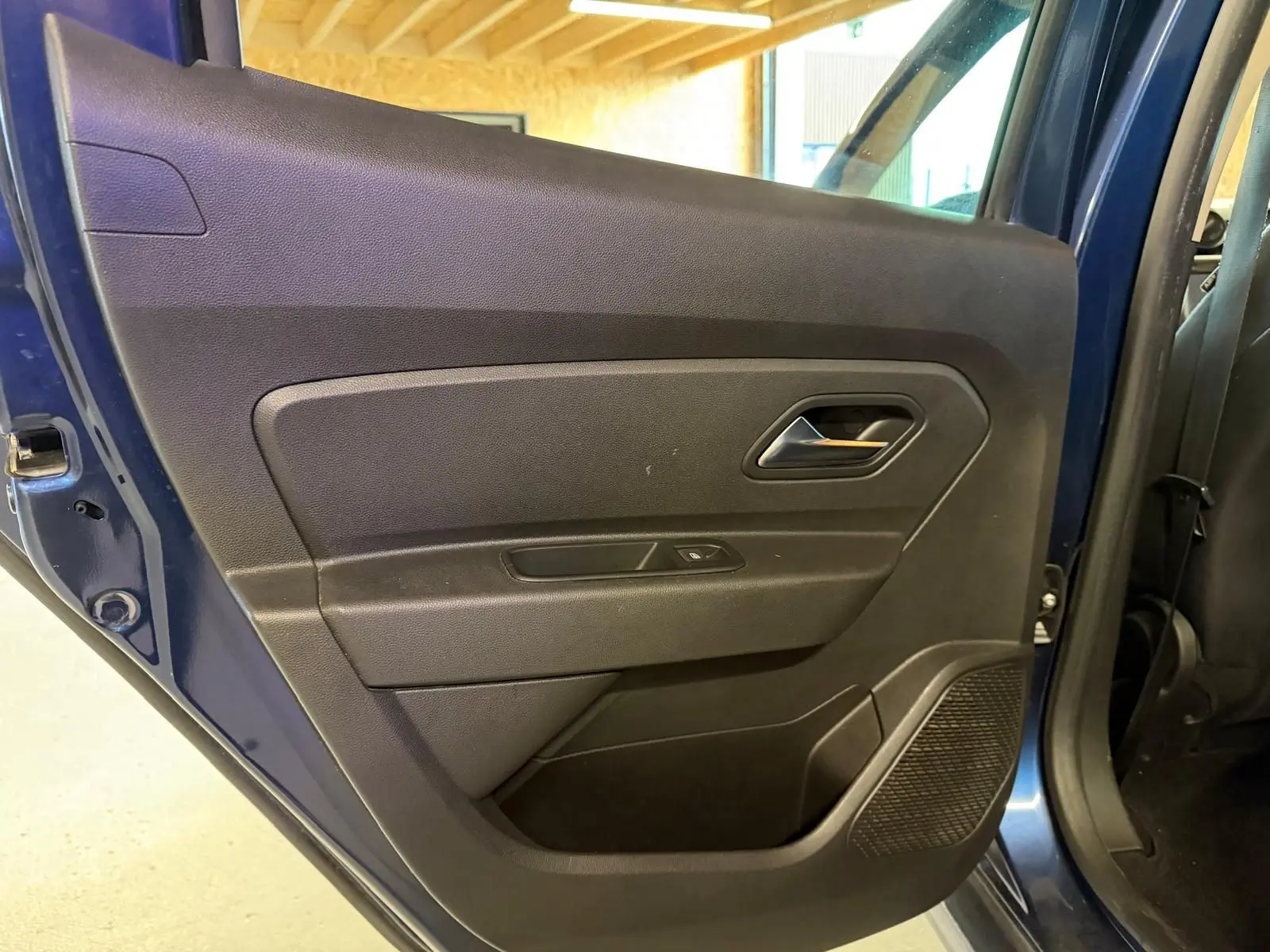 Gros plan sur la porte arrière gauche noire du Dacia Duster bleu, avec poignée et commande de vitre visible.