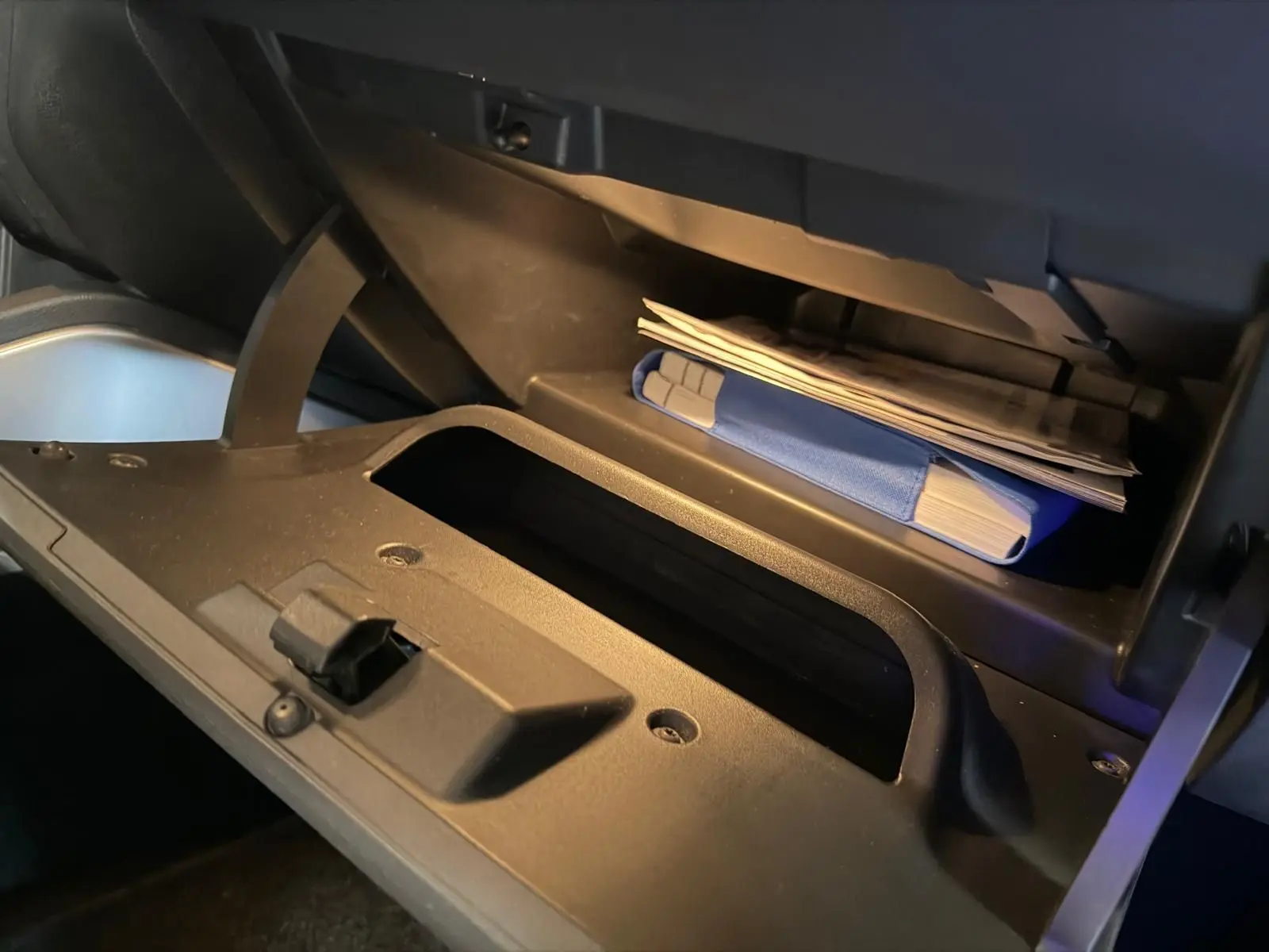 Gros plan sur la boîte à gants ouverte du Dacia Duster bleu, montrant des documents et un manuel rangés à l'intérieur.