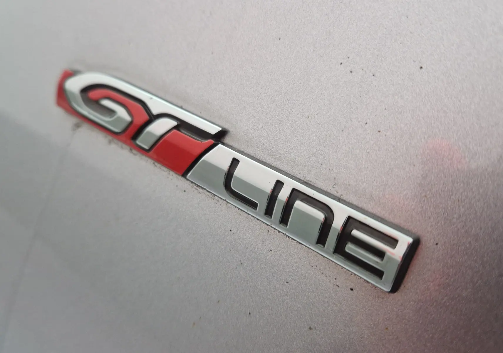 Gros plan sur l’inscription GT Line rouge et chrome sur la carrosserie gris Artense d’une Peugeot 308 SW.