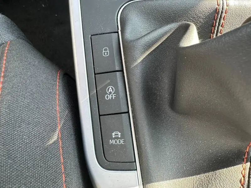 Gros plan sur la console centrale du SEAT Arona 2025, montrant les boutons de verrouillage, arrêt auto start/stop et mode conduite, avec coutures rouges.