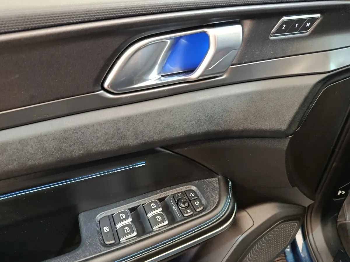 Détail de la porte côté conducteur du LINK & CO 01 bleu, avec poignée alu, surpiqûres bleues et commandes des vitres.