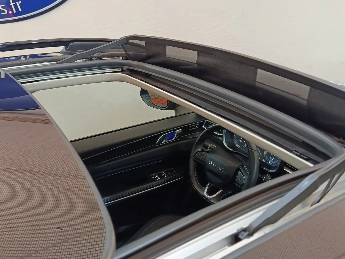 Vue intérieure par le toit ouvrant du volant cuir noir et tableau de bord digital du Lynk & Co 01 hybride rechargeable.