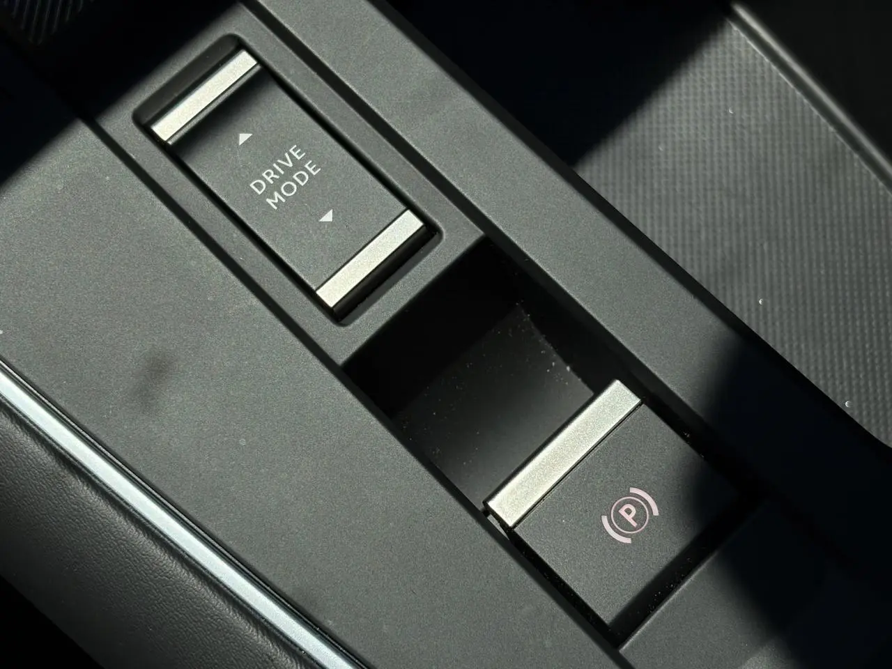 Gros plan sur la console centrale noire du Citroën C5 Aircross Hybrid 2025 avec bouton Drive Mode et frein de stationnement électrique.