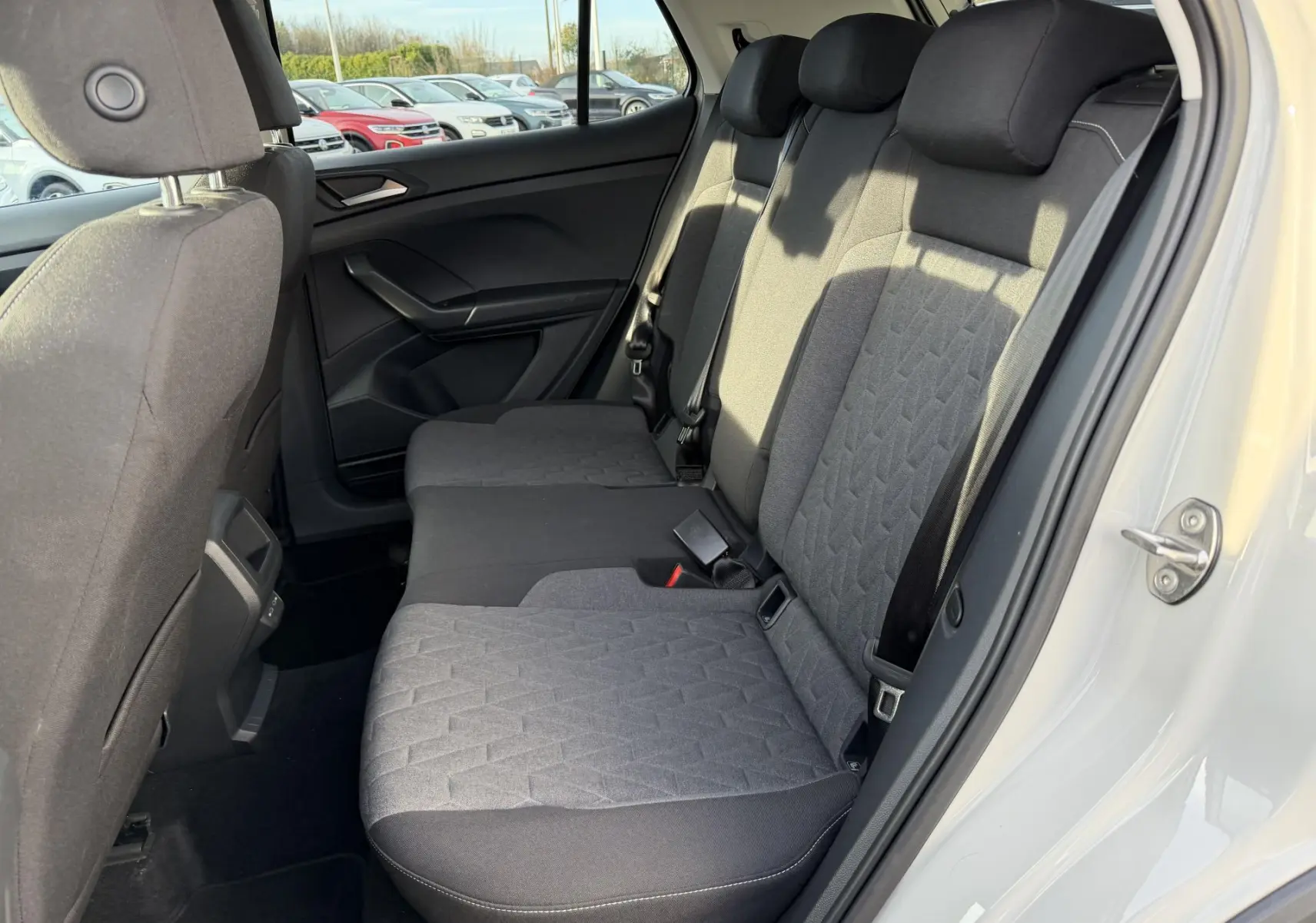 Vue côté droit de la banquette arrière grise du Volkswagen T-Cross 2025 avec sièges tissu bicolore et ceintures noires.