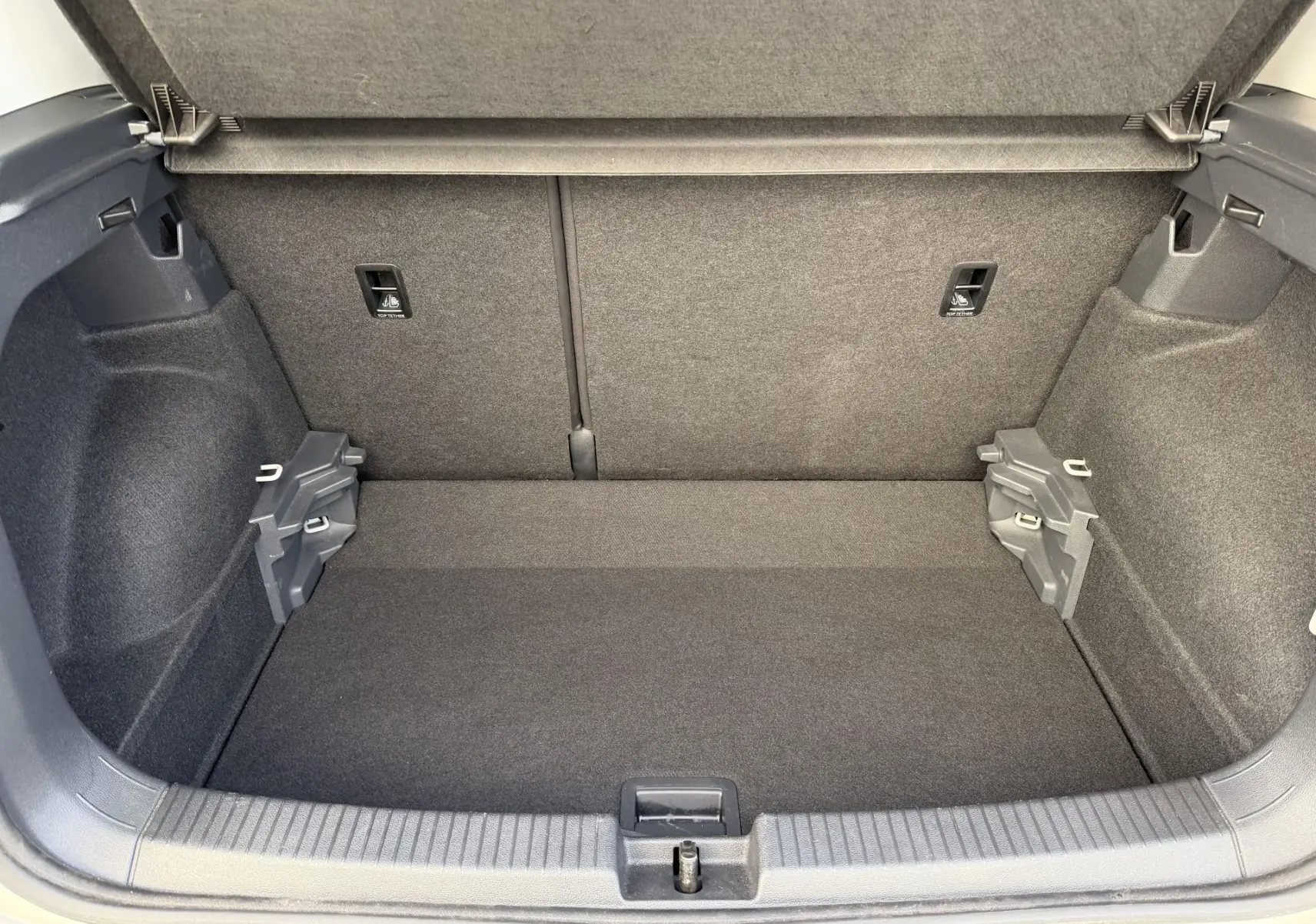 Coffre ouvert du Volkswagen T-Cross gris, vue de l'intérieur montrant un espace de rangement propre et bien fini.