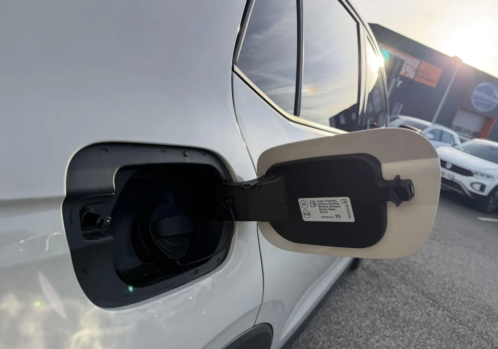 Gros plan sur la trappe à carburant ouverte côté gauche d'un Volkswagen T-Cross gris sous lumière naturelle.