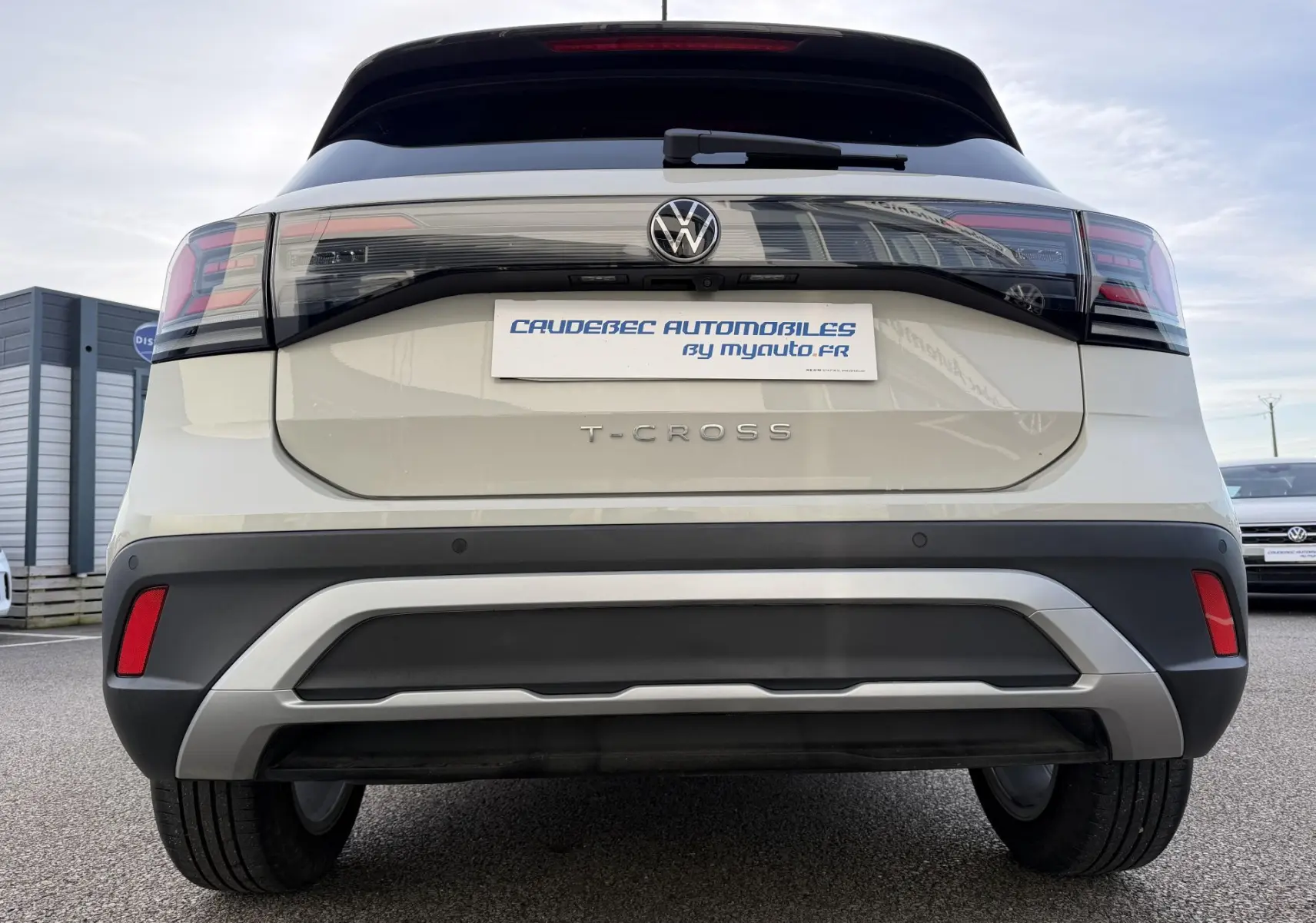 Vue arrière d'un Volkswagen T-Cross gris avec feux LED et logo VW visible sur un parking extérieur.