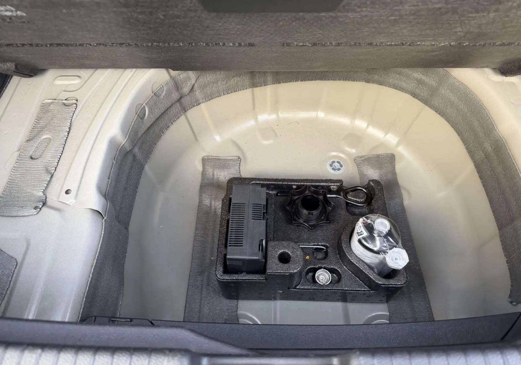 Vue plongeante sur le coffre ouvert d'un Volkswagen T-Cross gris, montrant le kit de dépannage sous le plancher.