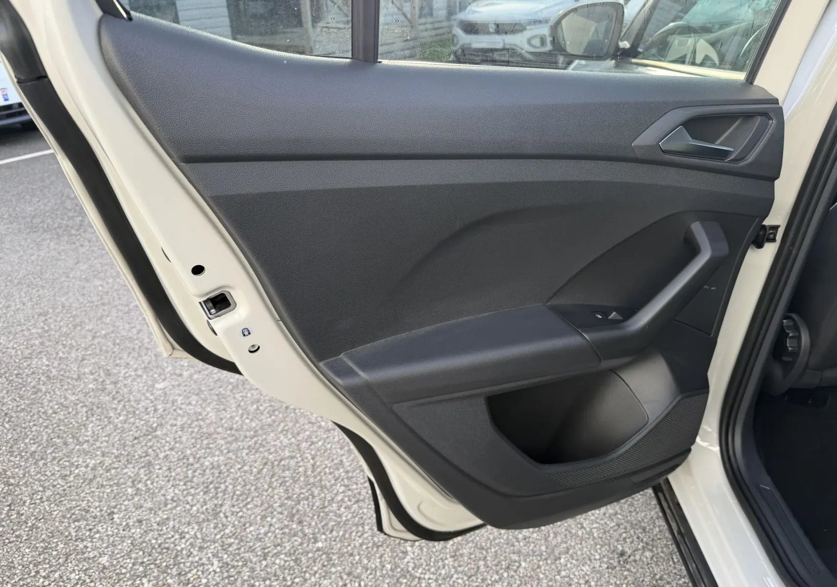 Vue intérieure de la porte arrière gauche noire du Volkswagen T-Cross 2025, avec poignée et commande de vitre visible.