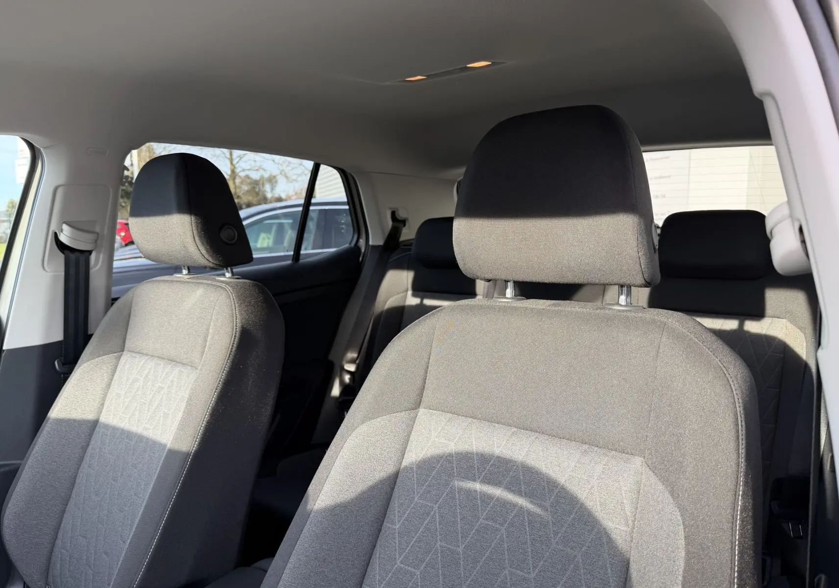 Vue intérieure sur les sièges avant gris tissu du Volkswagen T-Cross, avec banquette arrière partiellement visible.