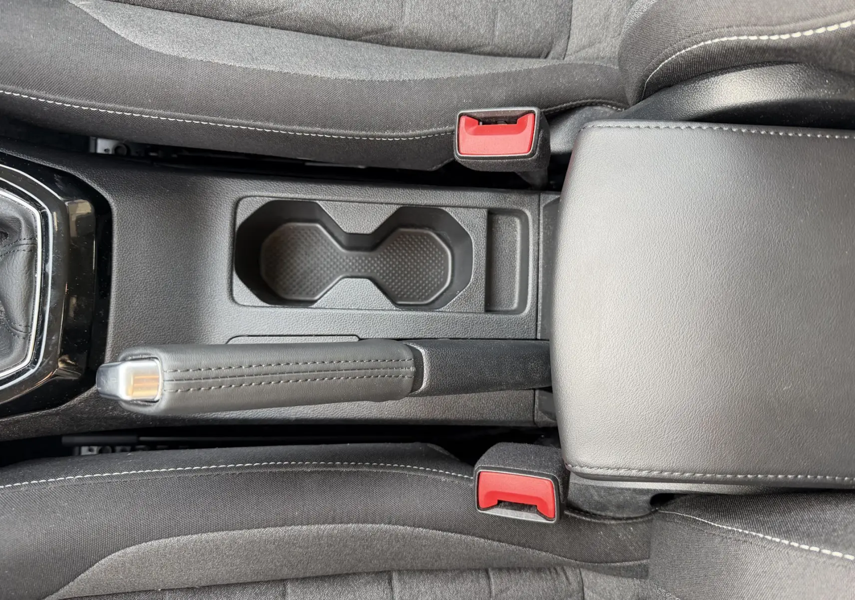 Vue plongeante sur la console centrale noire du Volkswagen T-Cross avec frein à main manuel et porte-gobelets.